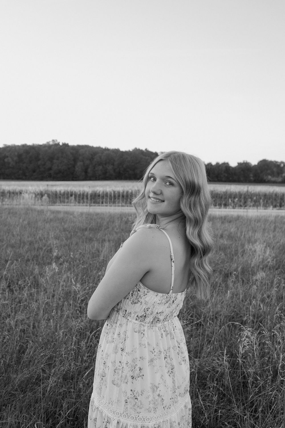 A person in a floral sundress poses in a serene meadow during golden hour.