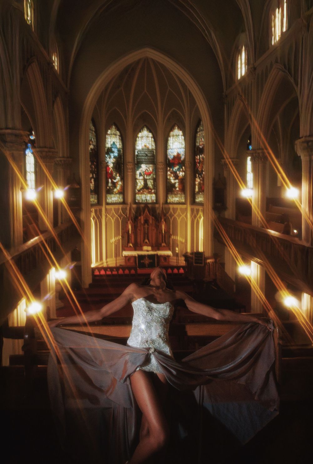 Dramatic fashion pose in a white dress against gothic church architecture and stained glass windows.