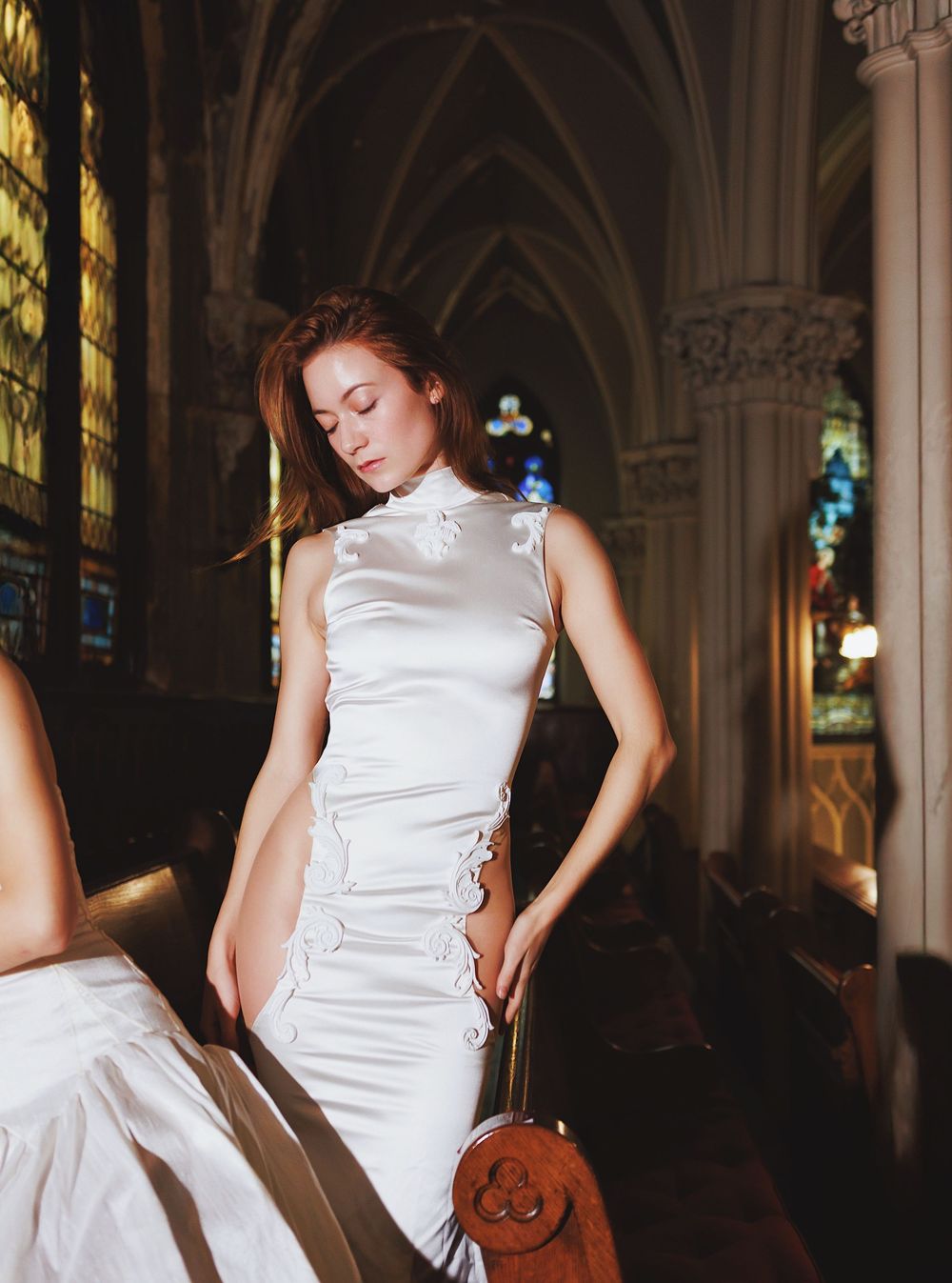 White formal dress contrasts against gothic cathedral arches and stained glass windows.