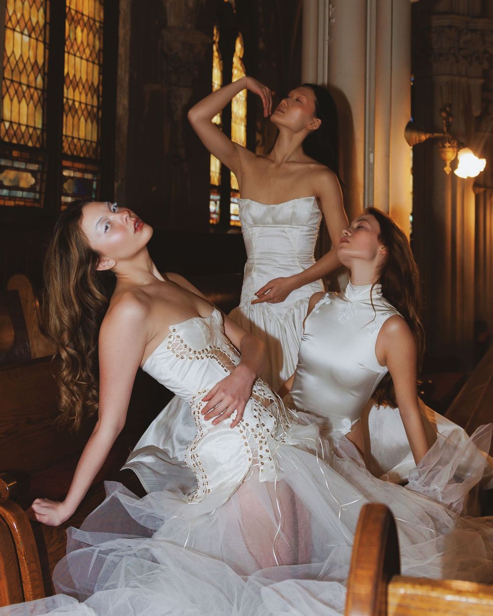 Three dancers in white dresses pose dramatically in an ornate church setting.