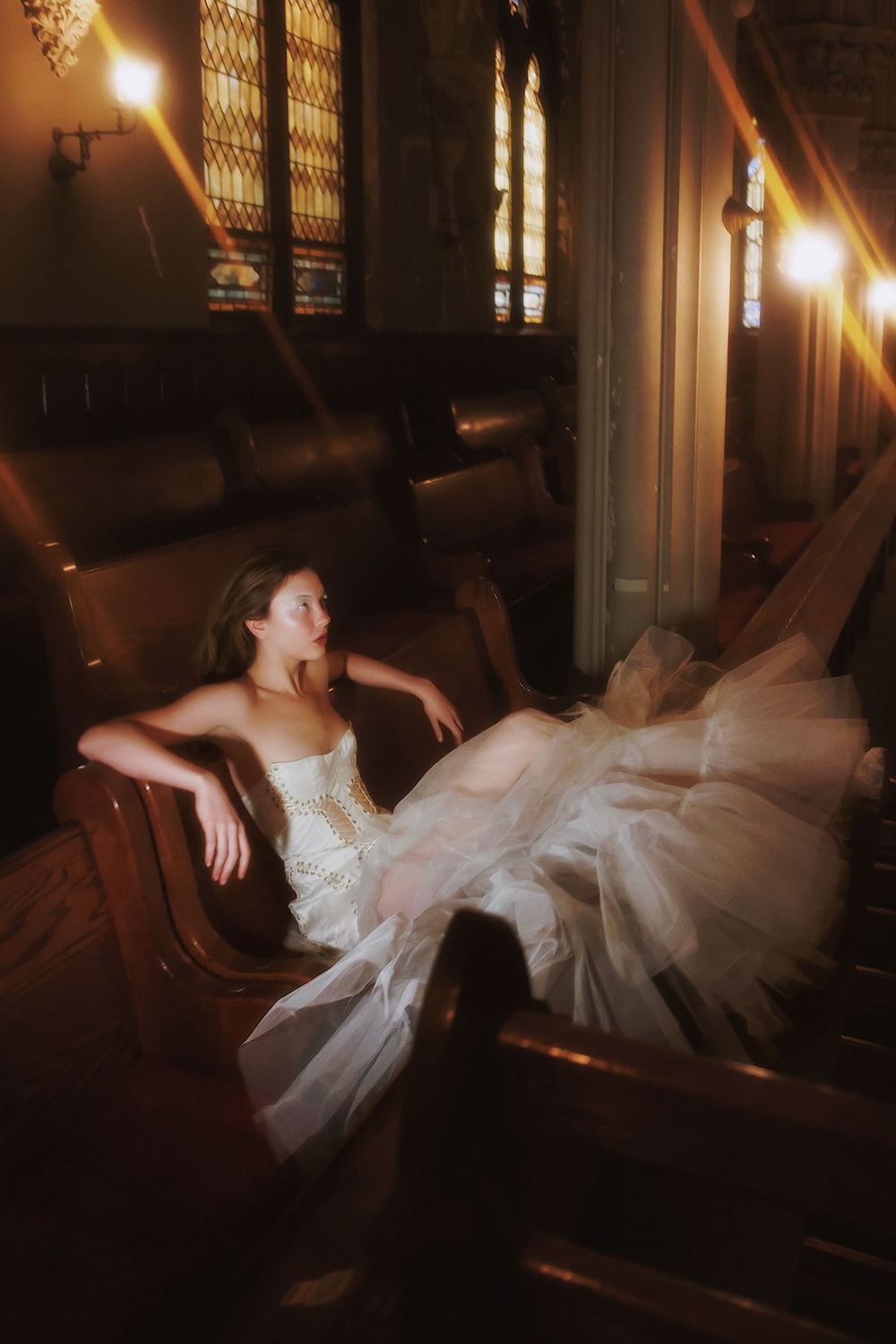 Ethereal bridal photo with sweeping white gown in church pews under warm lighting.
