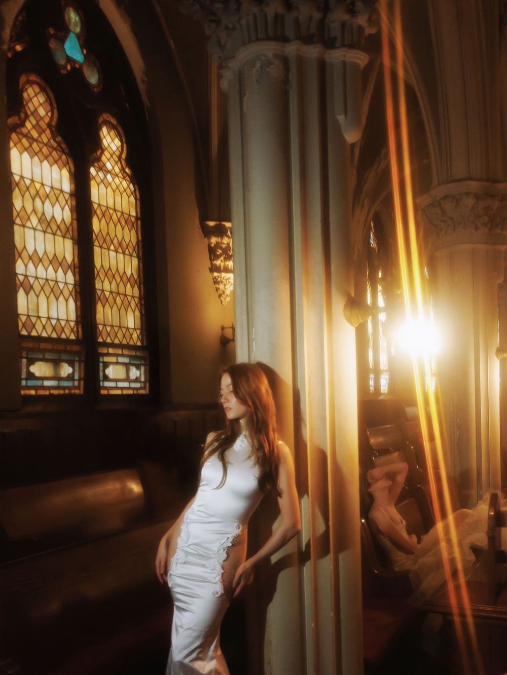Dramatic lighting illuminates stained glass windows in a church as a white dress stands in contrast.