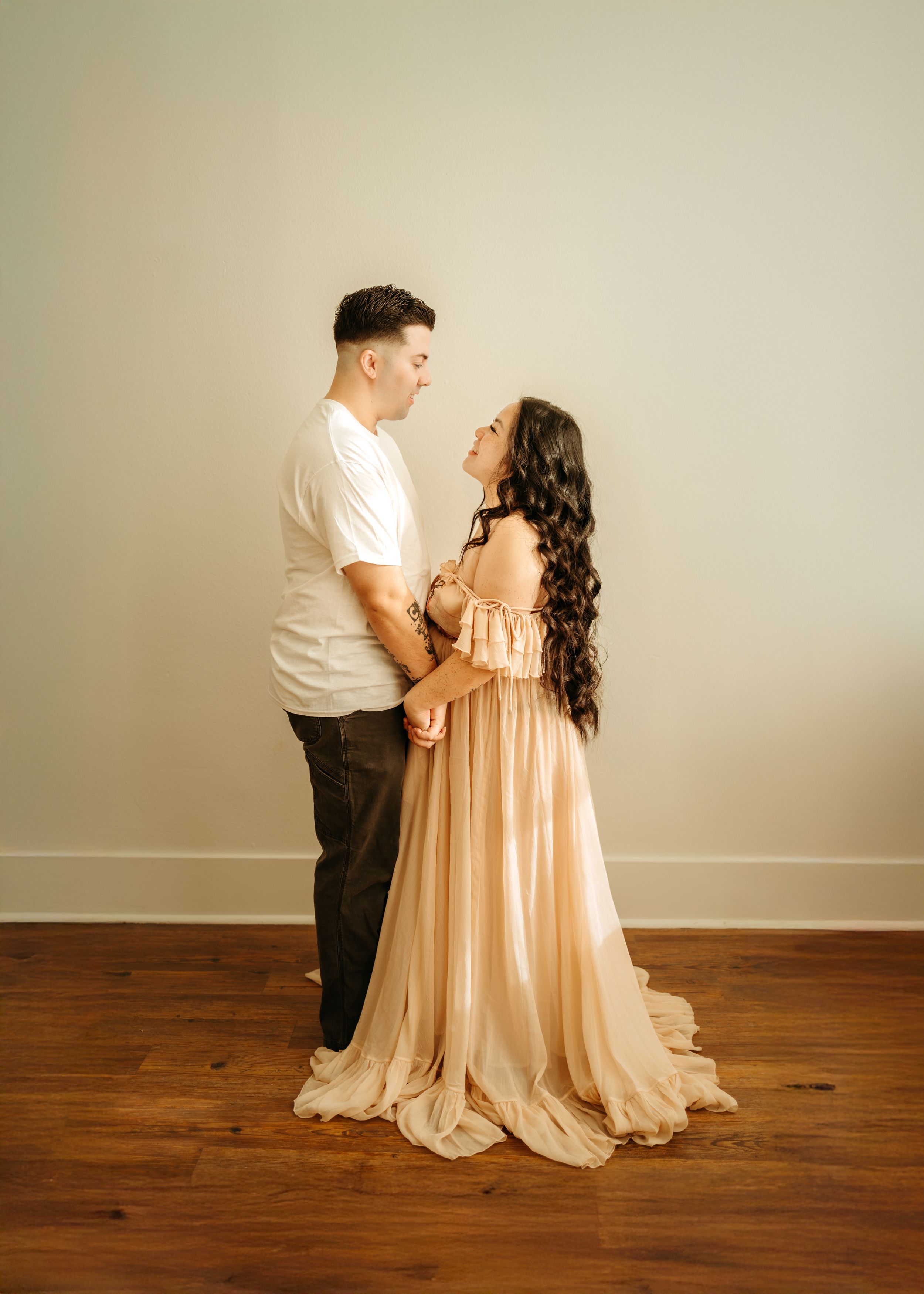 A couple in formal attire embraces in a romantic sequence of poses against a neutral backdrop with wooden floors.