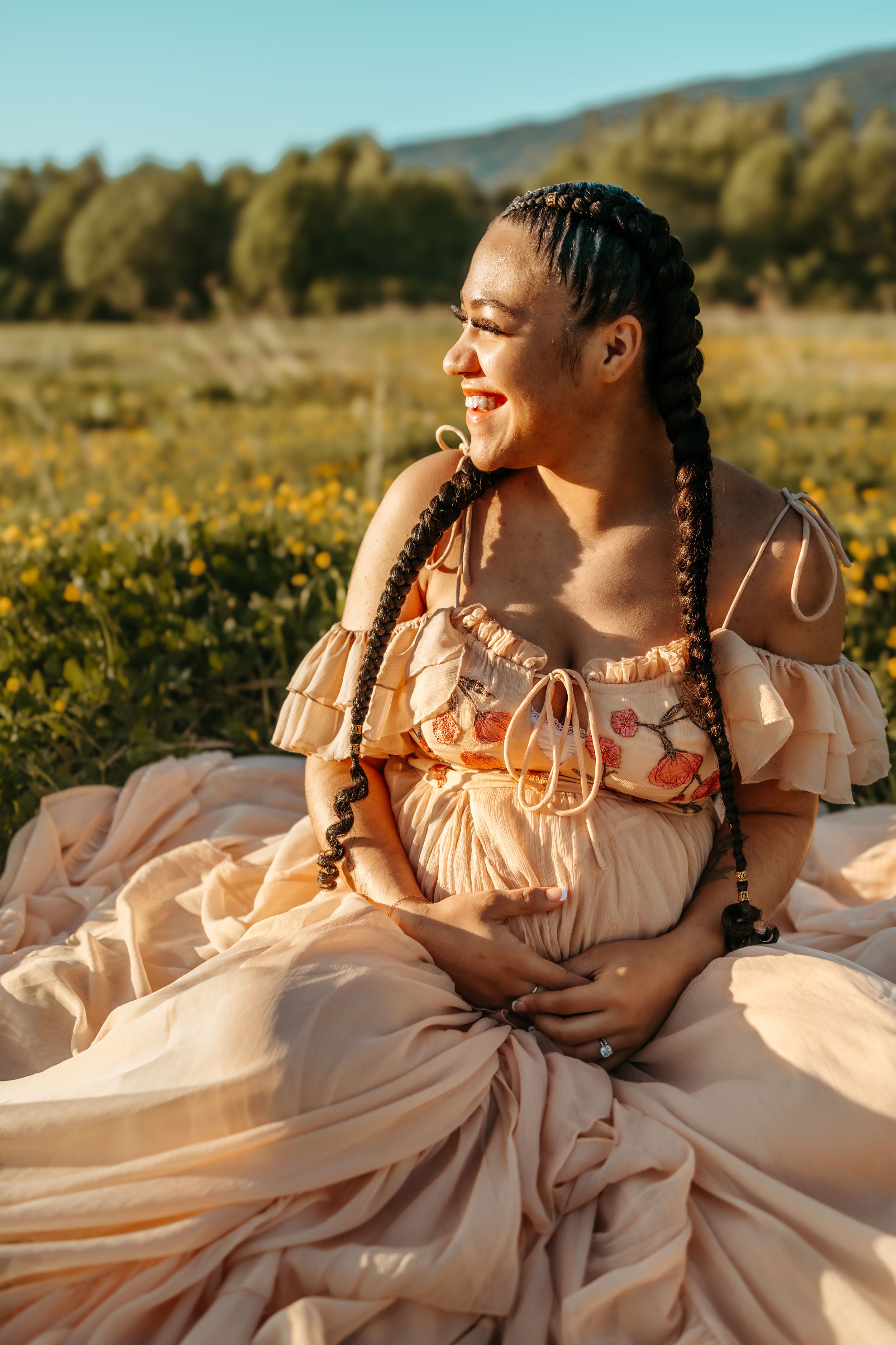 A person in a flowing peach dress lies in a sunlit meadow with golden wildflowers during sunset.