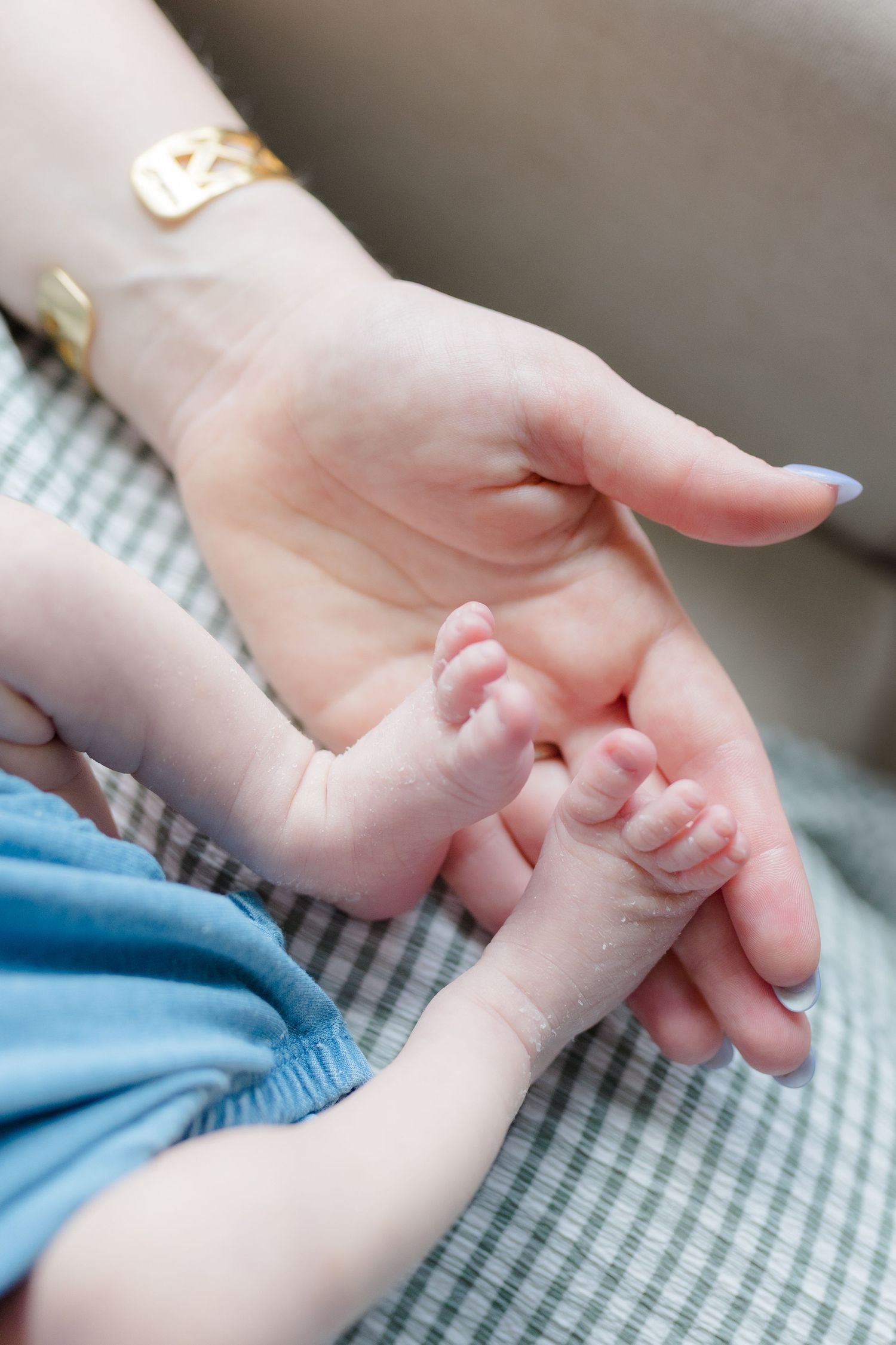 Delicate newborn baby fingers wrapped around an adult hand on a textured blanket.