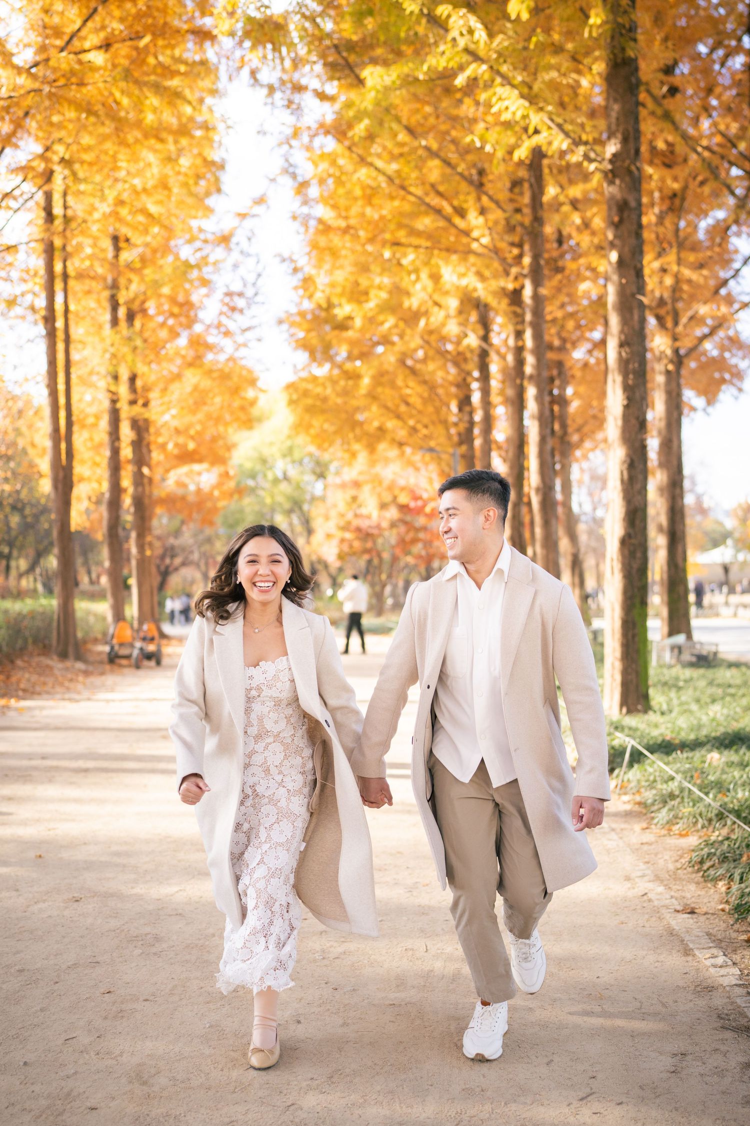 A couple in traditional Korean hanbok attire poses together in a park during golden hour.