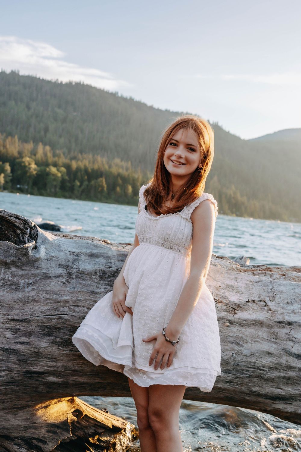White lace dress contrasts against rocky shoreline during golden hour photoshoot.