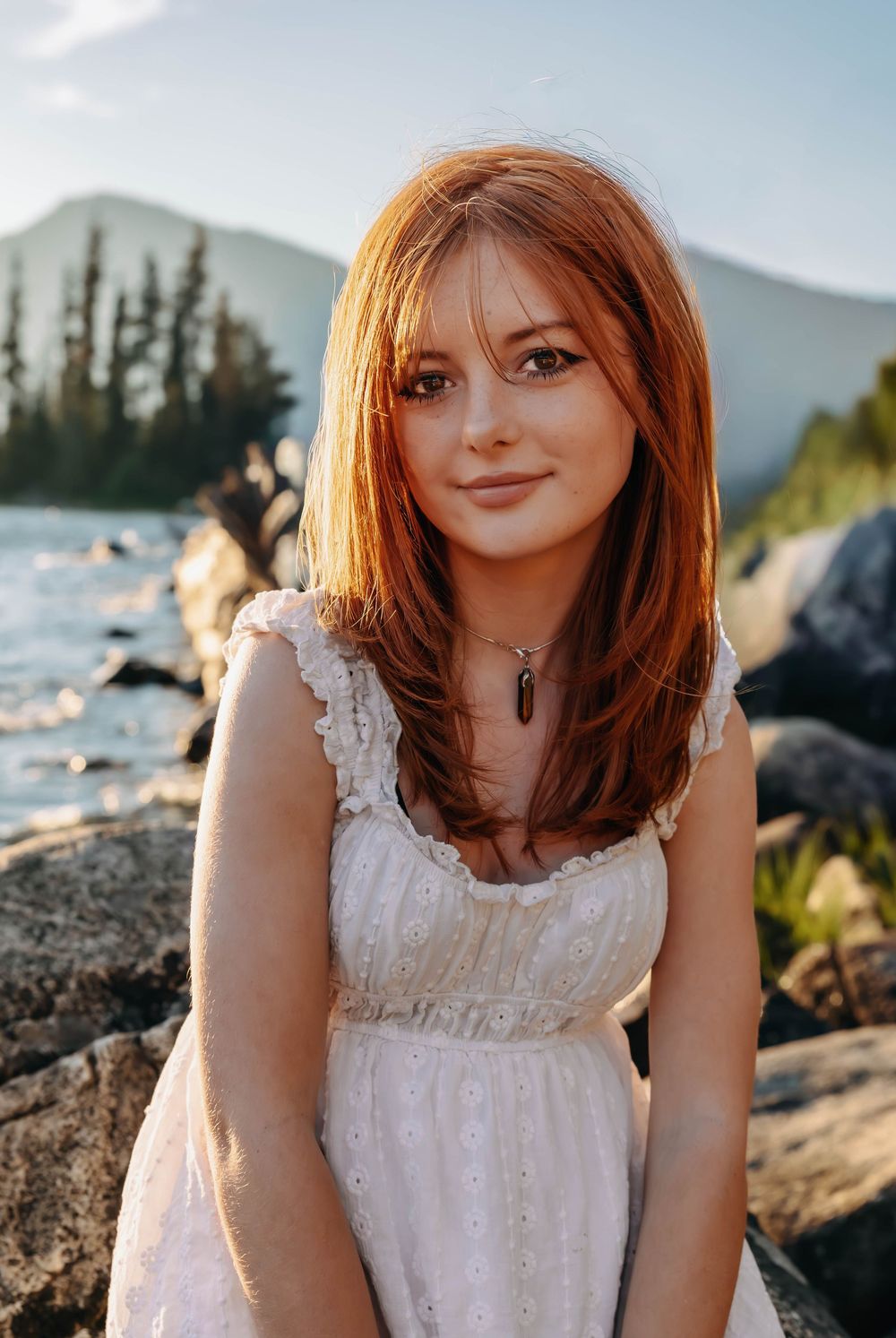 A white dress and necklace complement the mountain landscape backdrop.