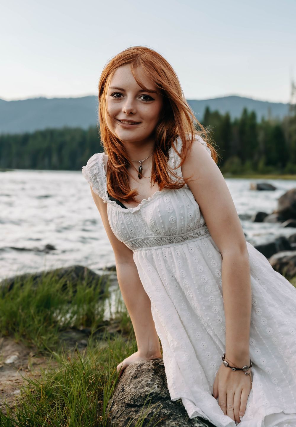 White dress contrasts beautifully against rocky shoreline and mountain vista.