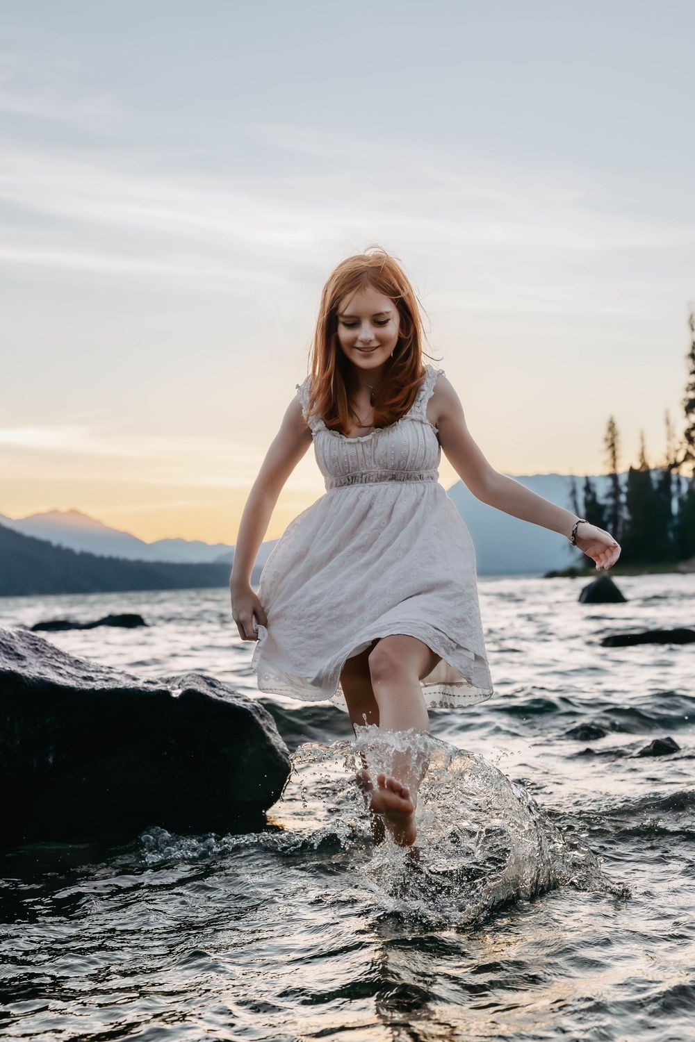 Splashing through mountain lake water in a flowing white dress at sunset.
