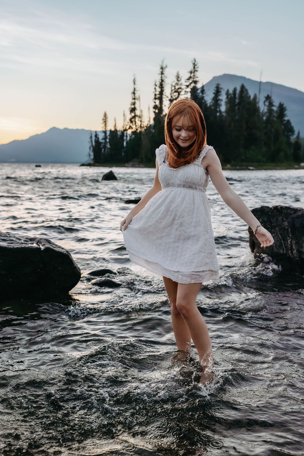 Playful moment captured splashing in mountain lake water wearing white dress.