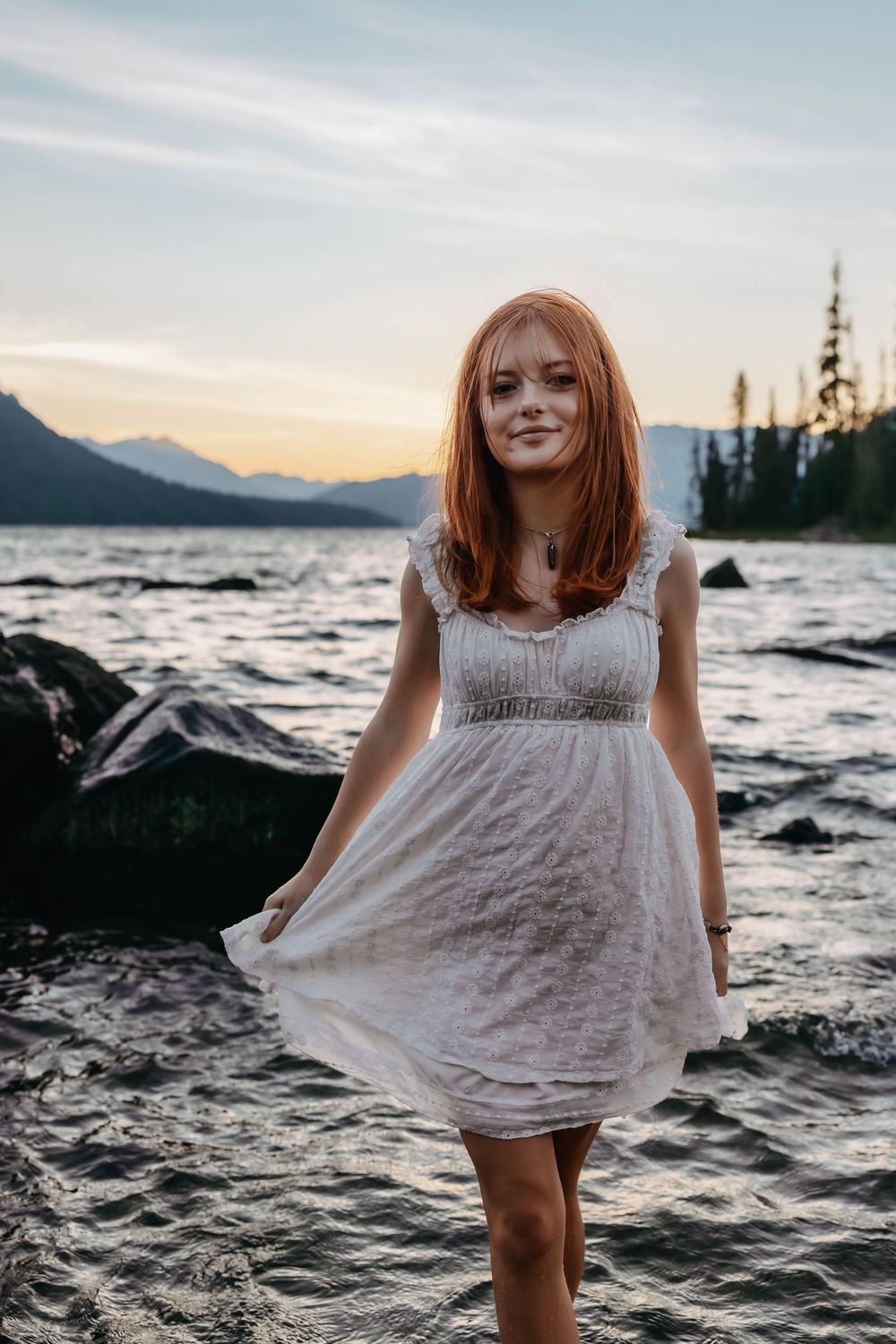 White dress flows in the breeze against mountain lake backdrop at golden hour.