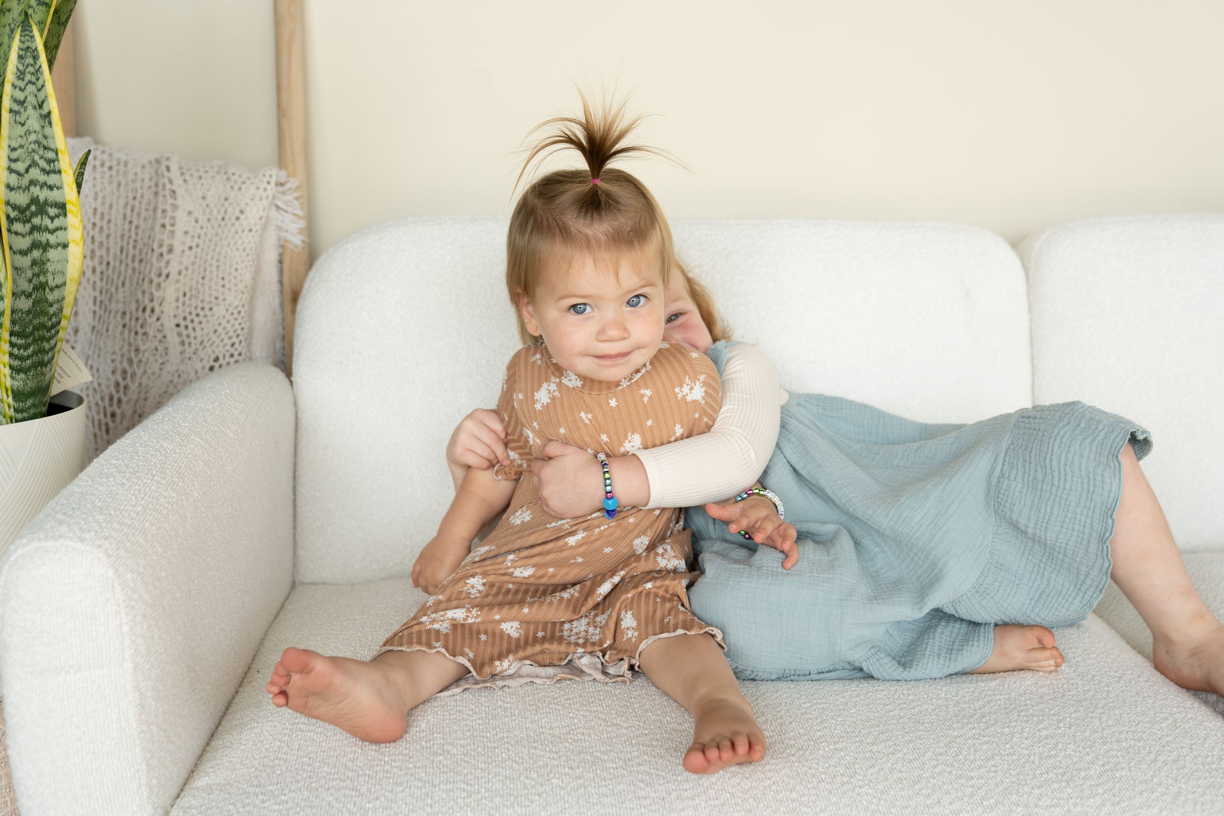 Two children lounging on white sofa wearing casual dresses in earth tones.