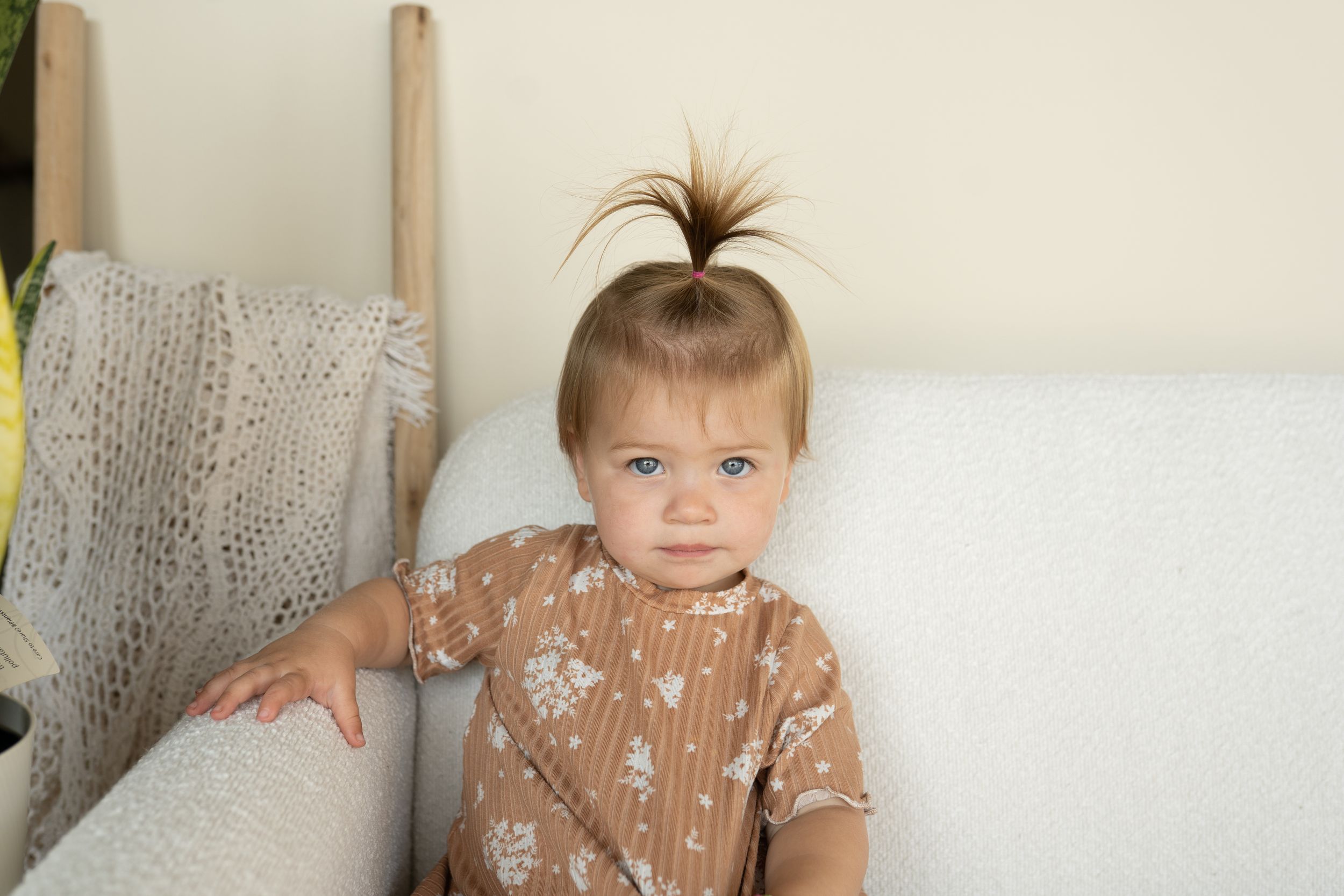 A small child in a brown floral dress sitting on a white couch.