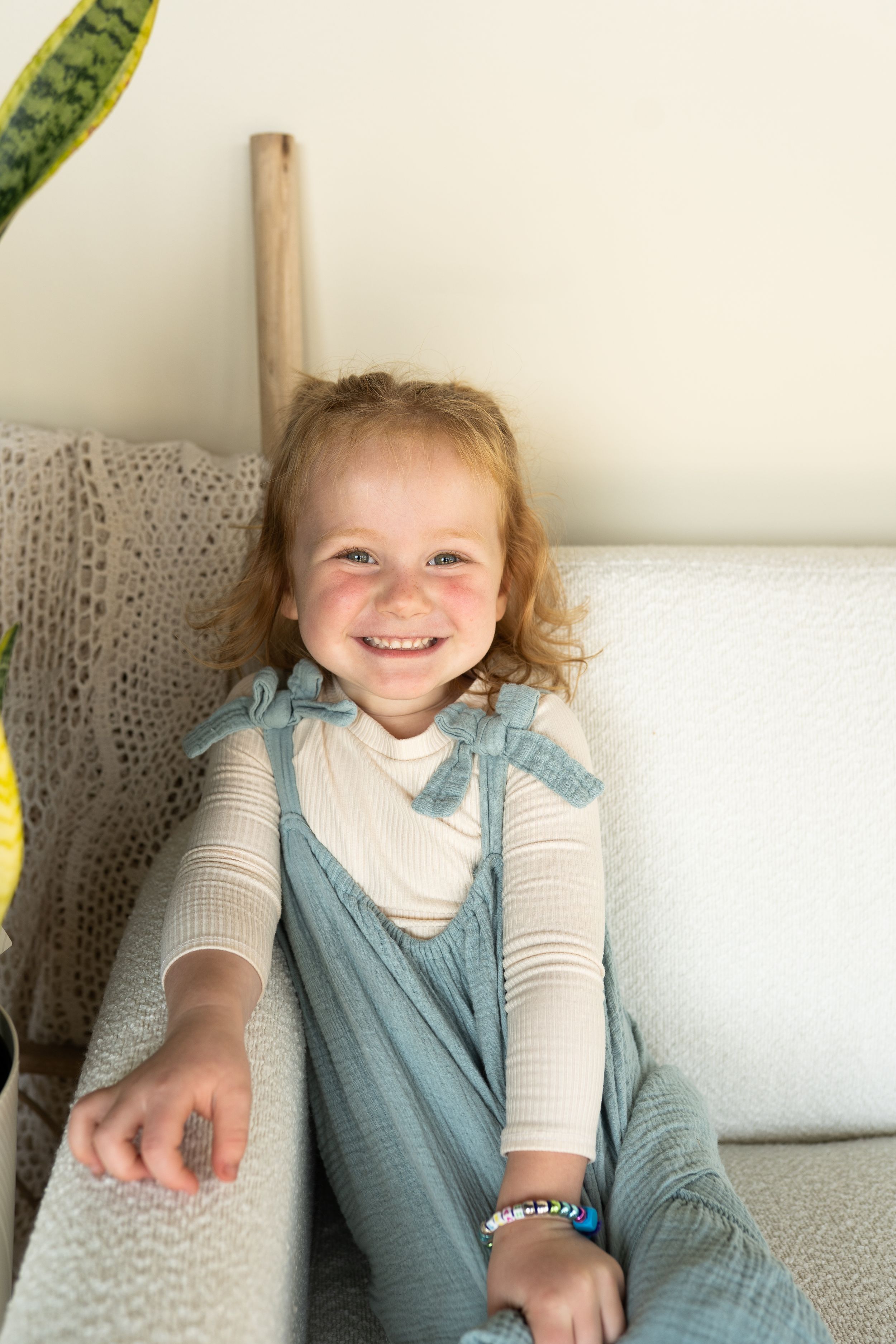 A child in a blue dress and white shirt smiling while sitting on a white couch.