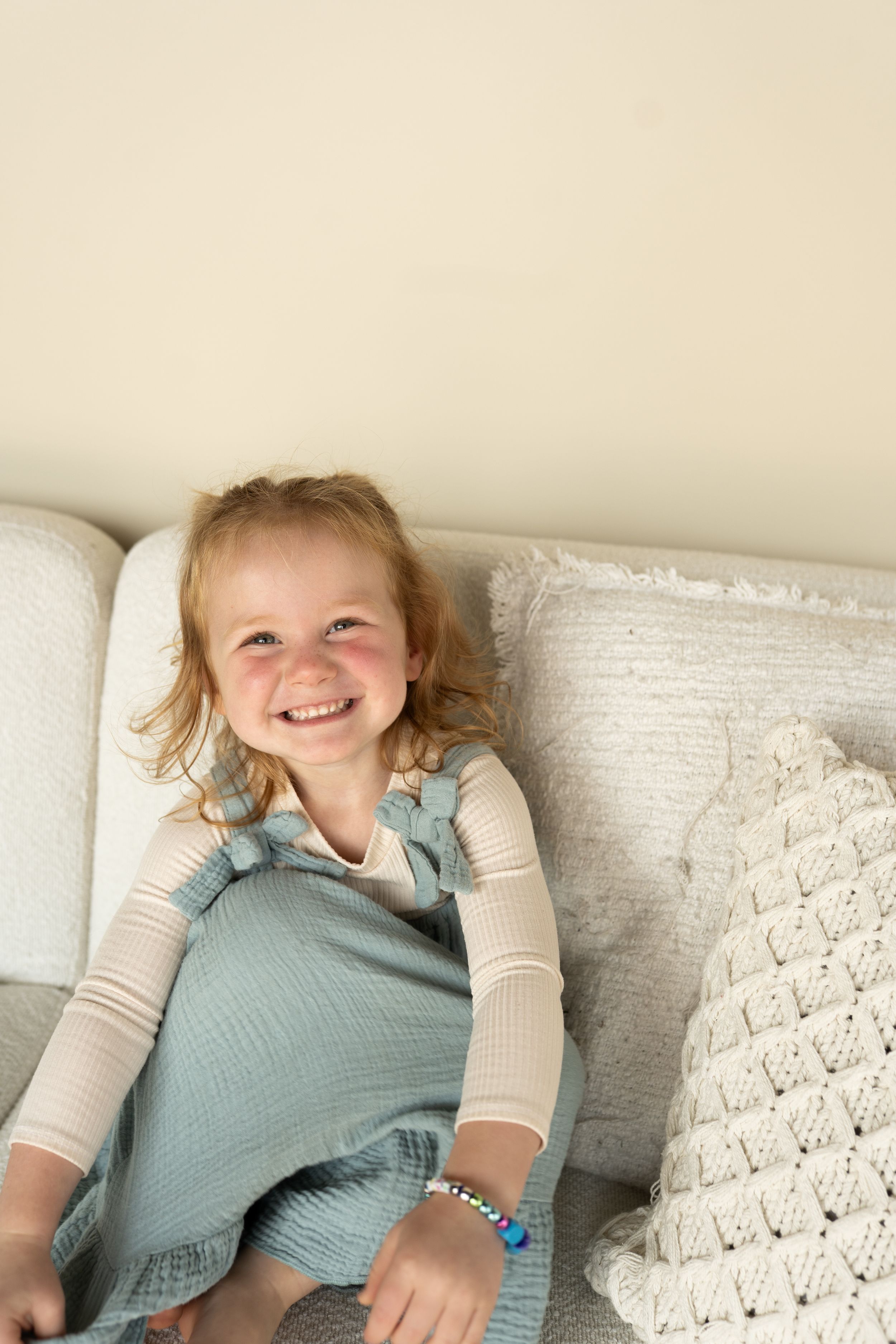 A joyful child in a blue dress and white shirt lounging on a couch with decorative pillows.