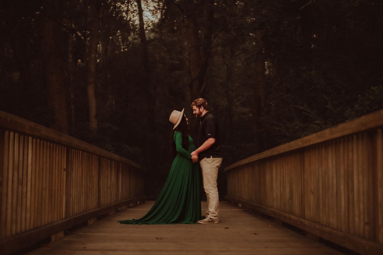 A couple in romantic forest setting with flowing green maternity dress and hat during a Rockingham, NC maternity session with Miranda Jo