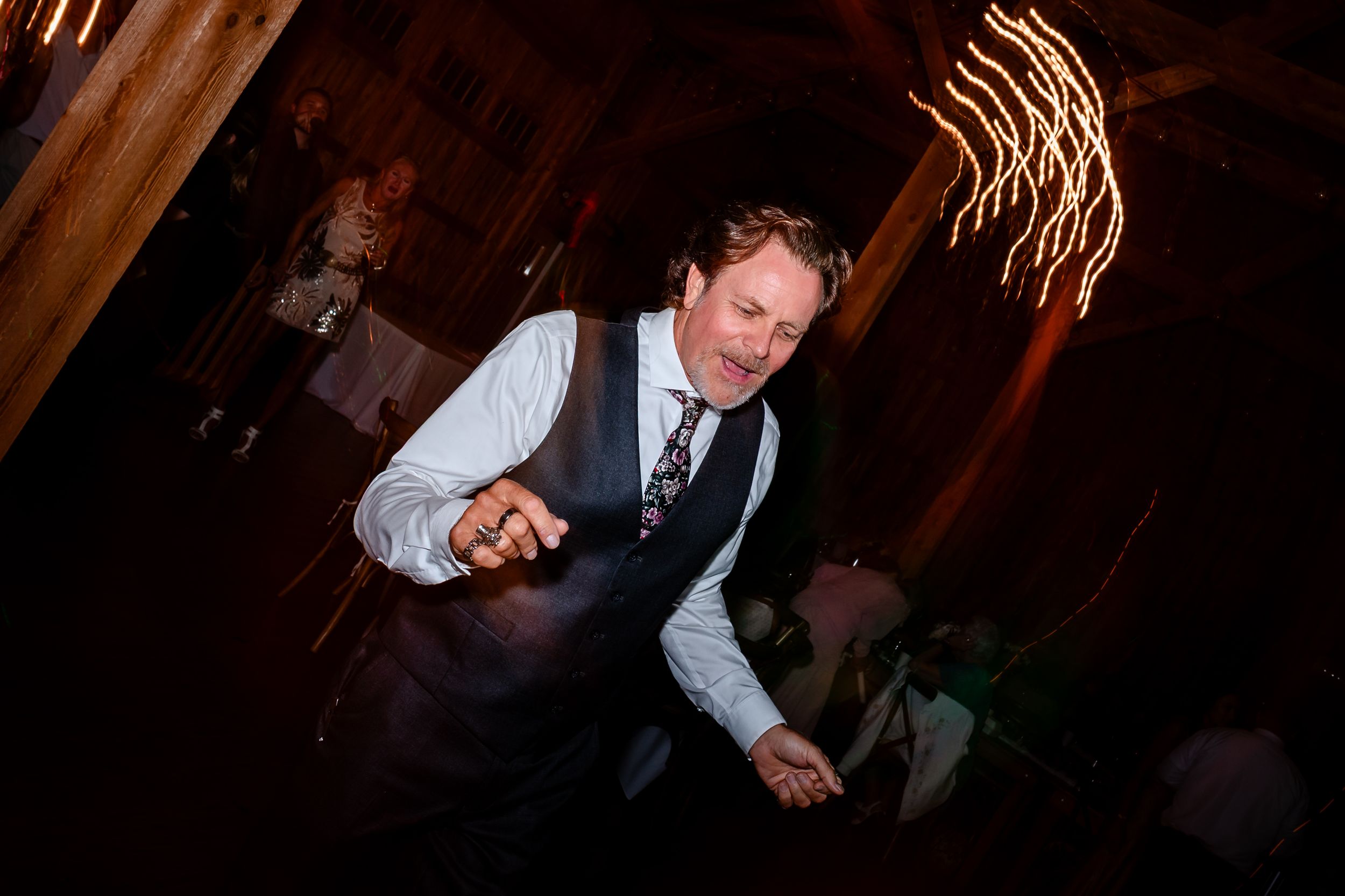 Wedding guests dancing energetically in a rustic wooden barn venue.