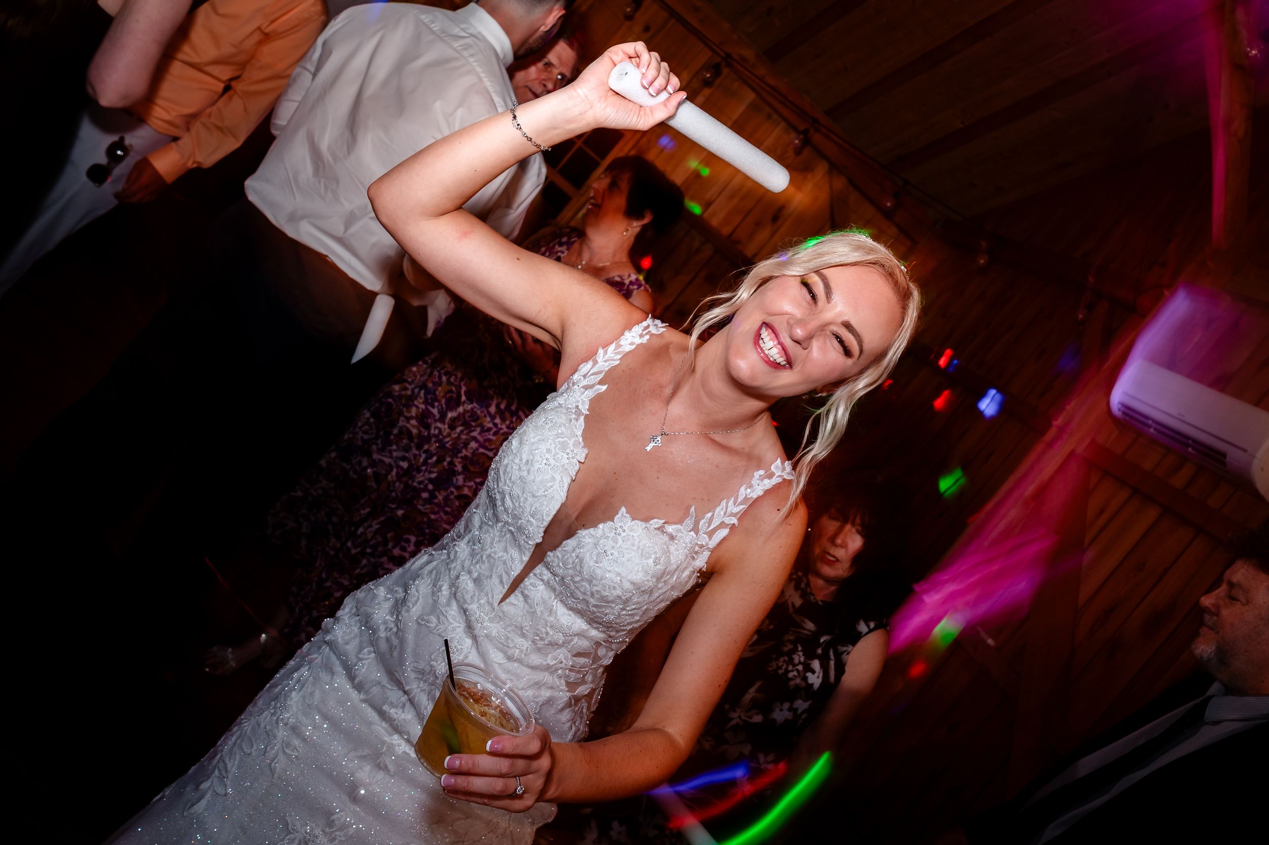 Wedding celebration with dancing and colorful lighting in rustic barn setting.