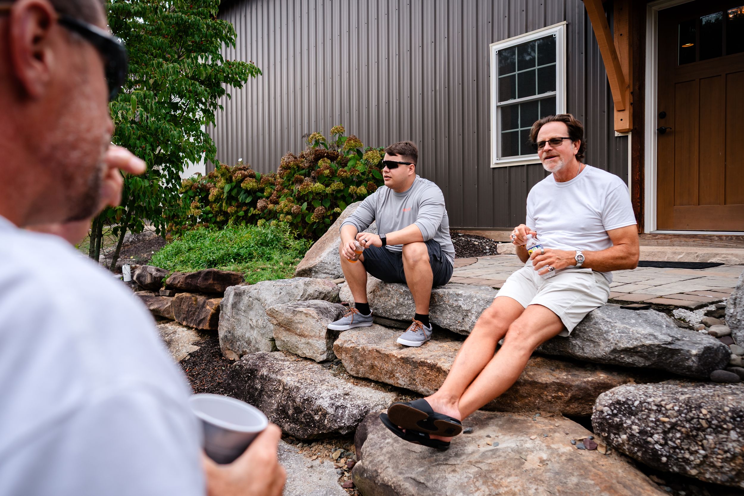 People relaxing on large decorative rocks outside a building with metal siding.