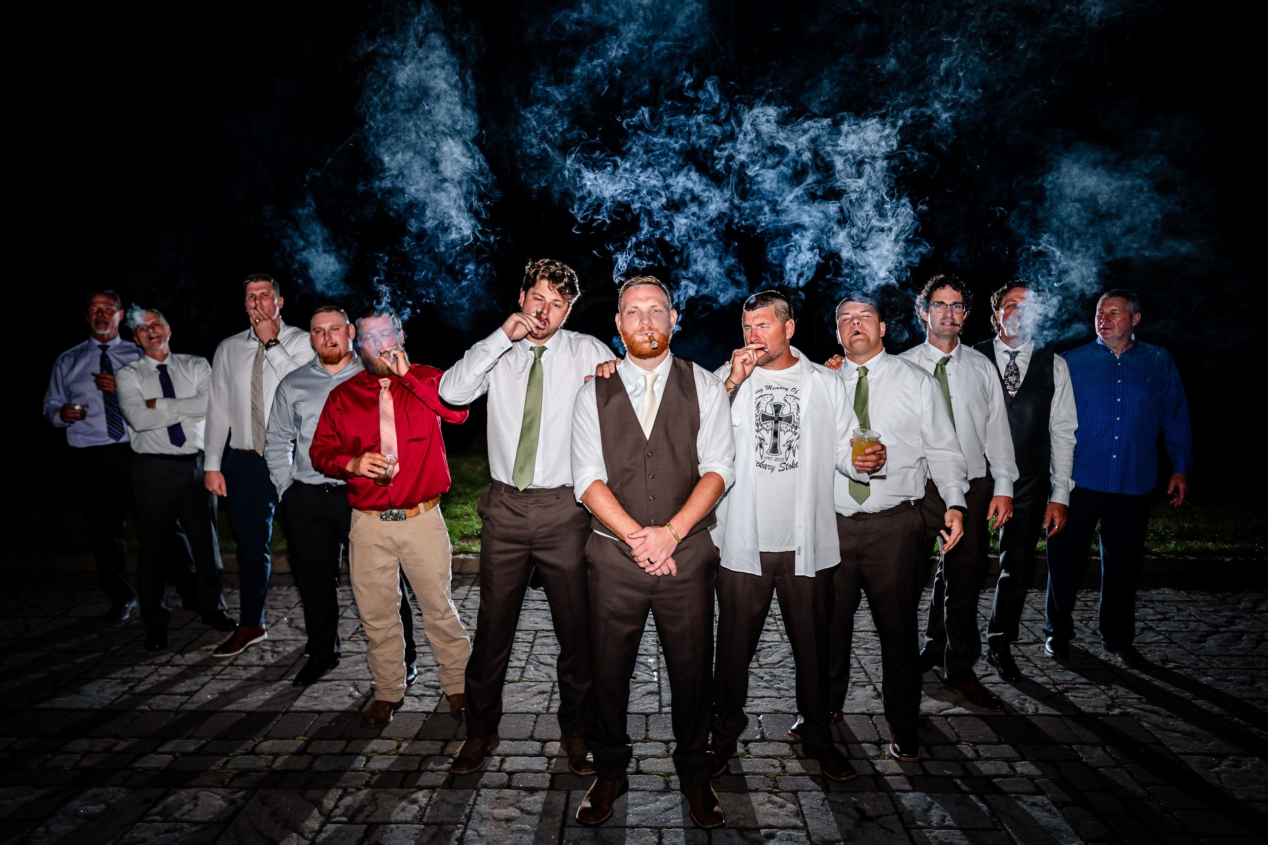 Wedding party members standing in a line at dusk creating silhouettes against a dark background.