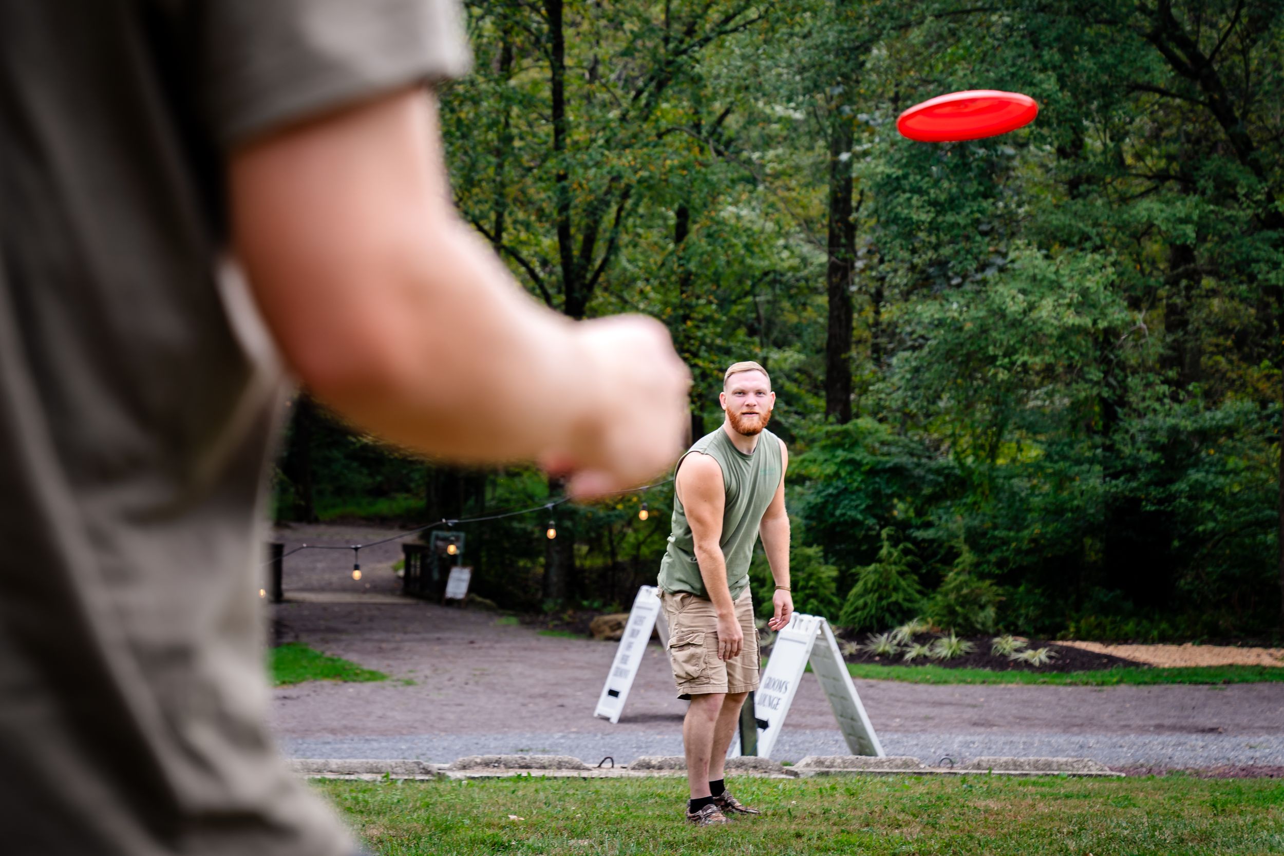 A red frisbee flying through the air in a wooded park setting.