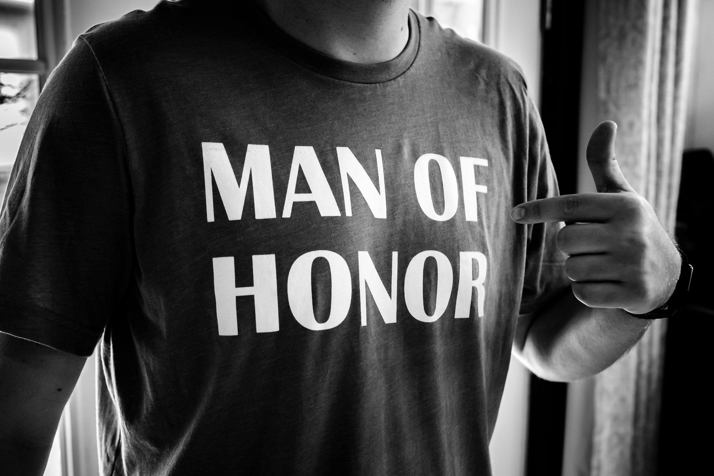 Close-up of a black t-shirt with 'Man of Honor' text printed in white letters.