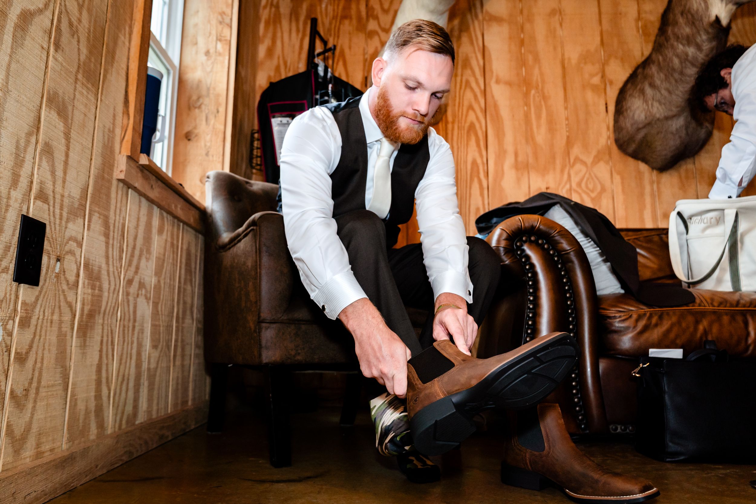 Someone adjusting formal footwear while getting dressed in a wooden room.