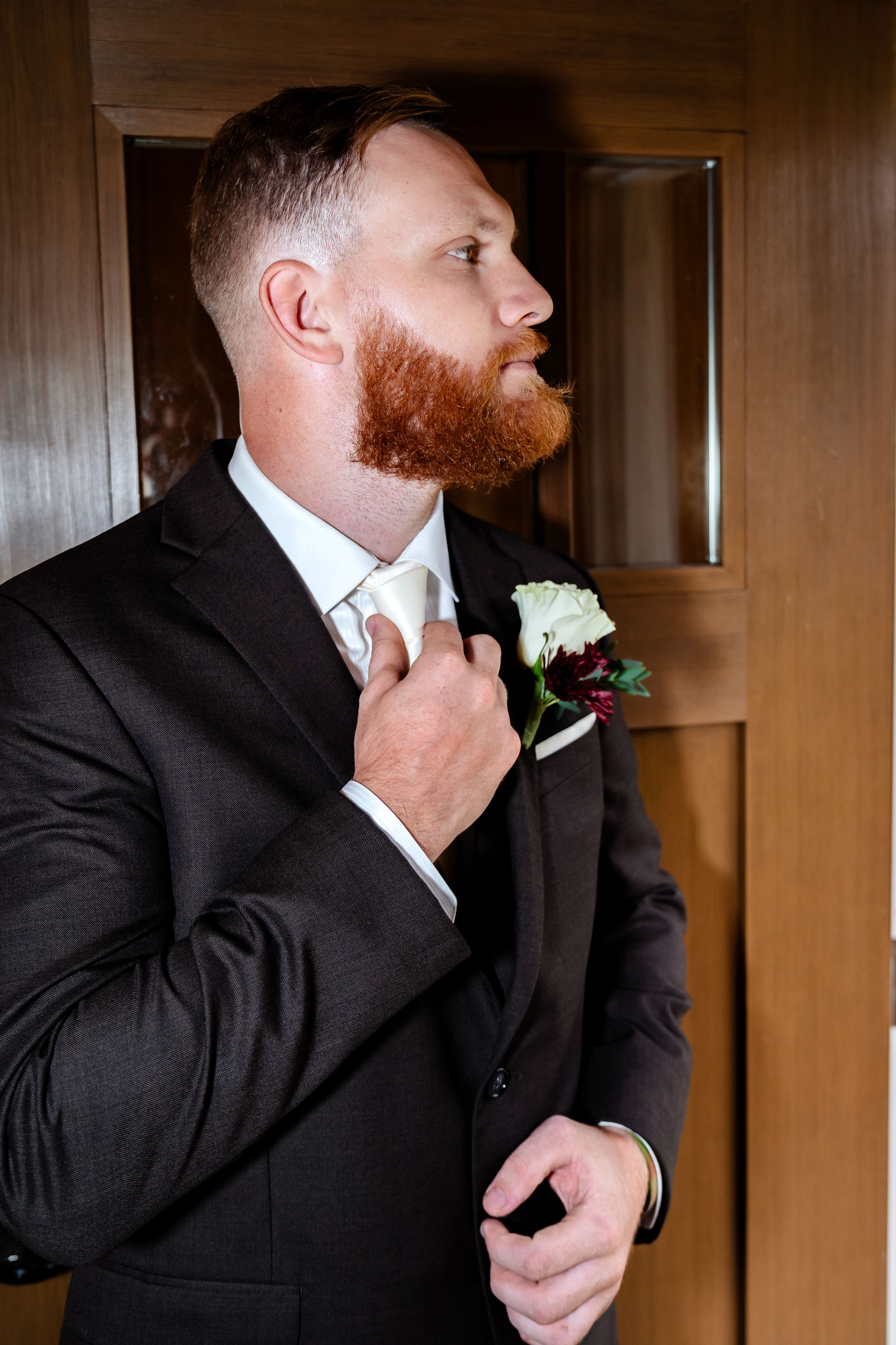 Side profile of someone in a dark suit adjusting a boutonniere.