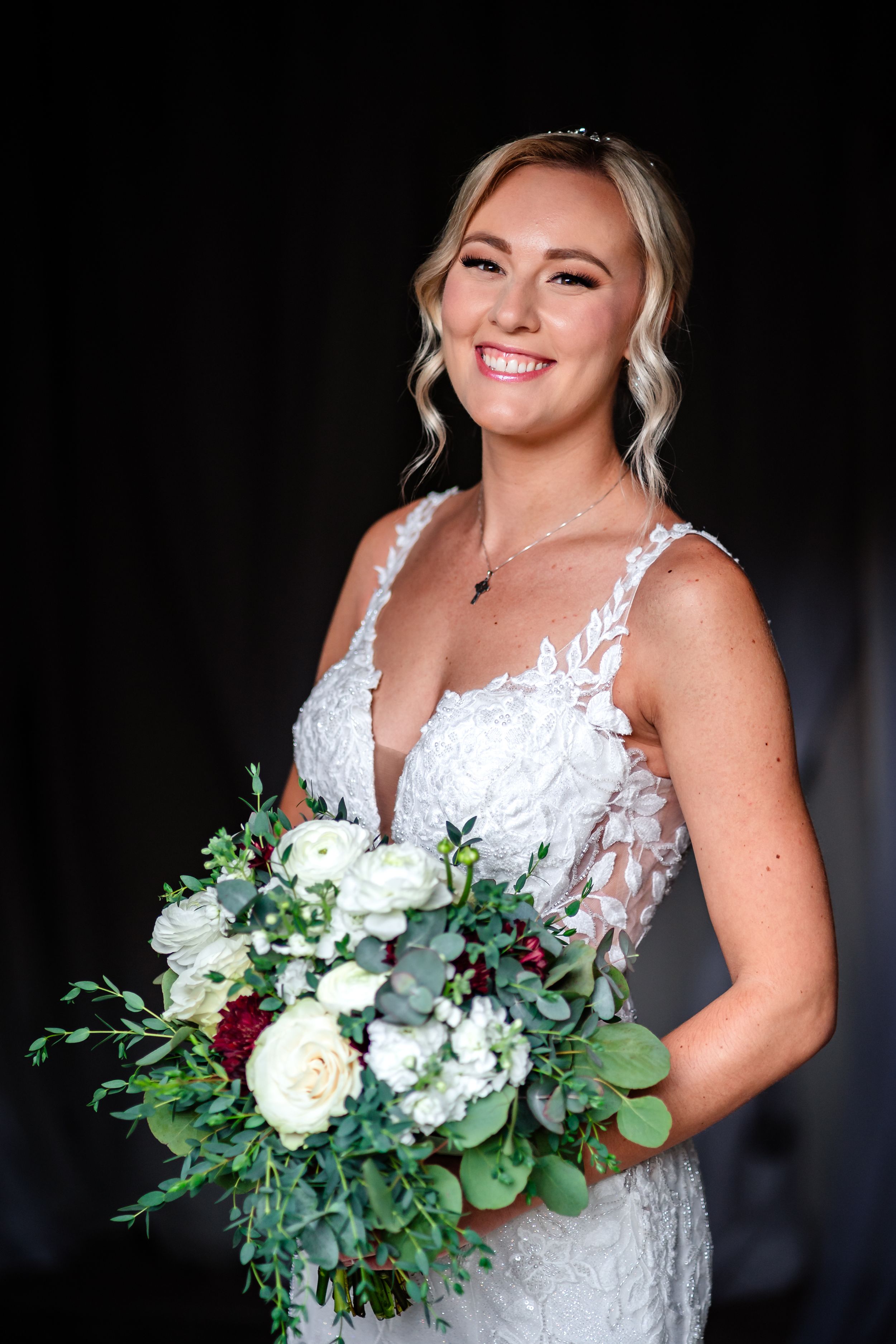 A bride in a white lace dress holds a bouquet with white flowers and greenery.
