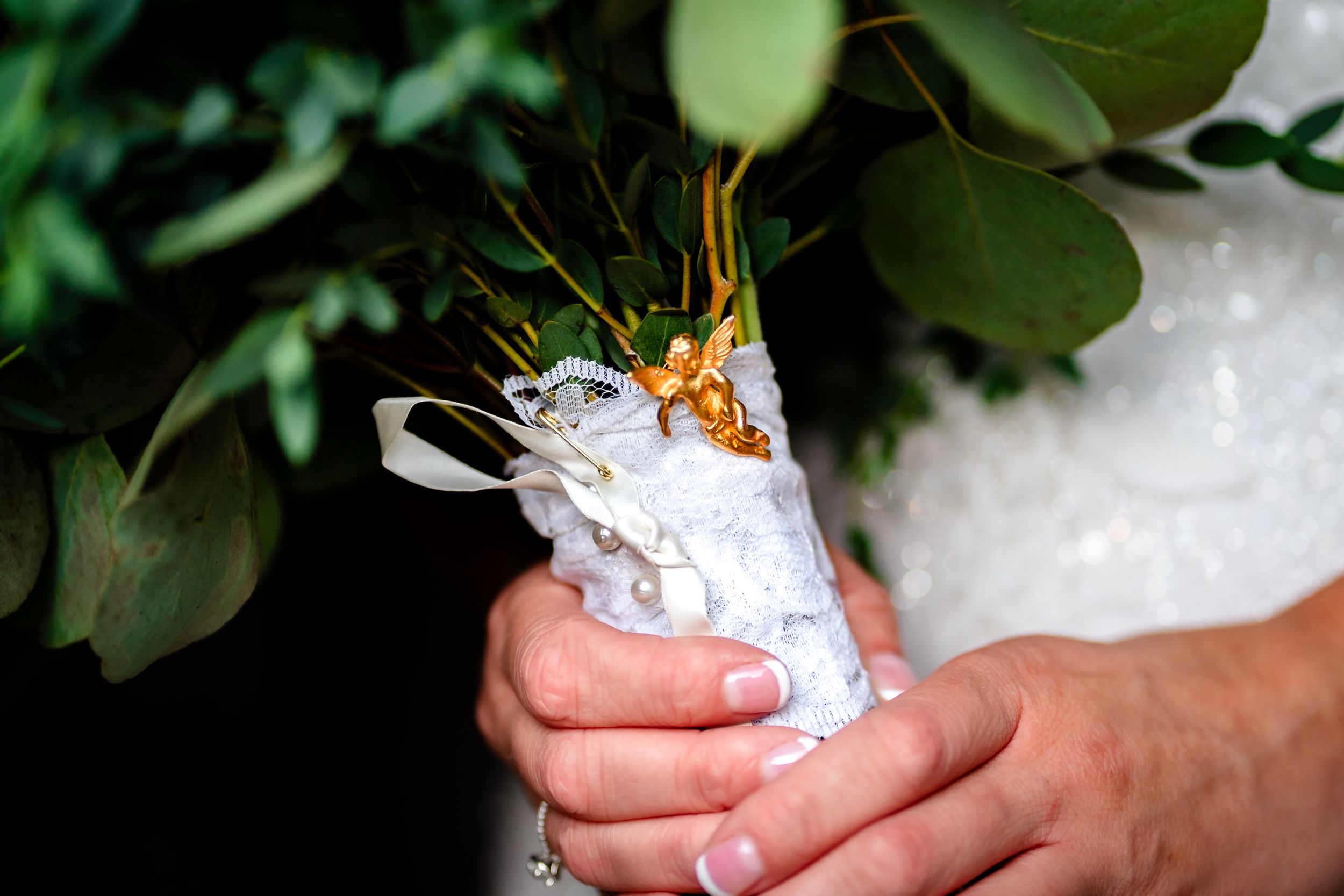 Hands holding a white decorated wedding shoe against green foliage.