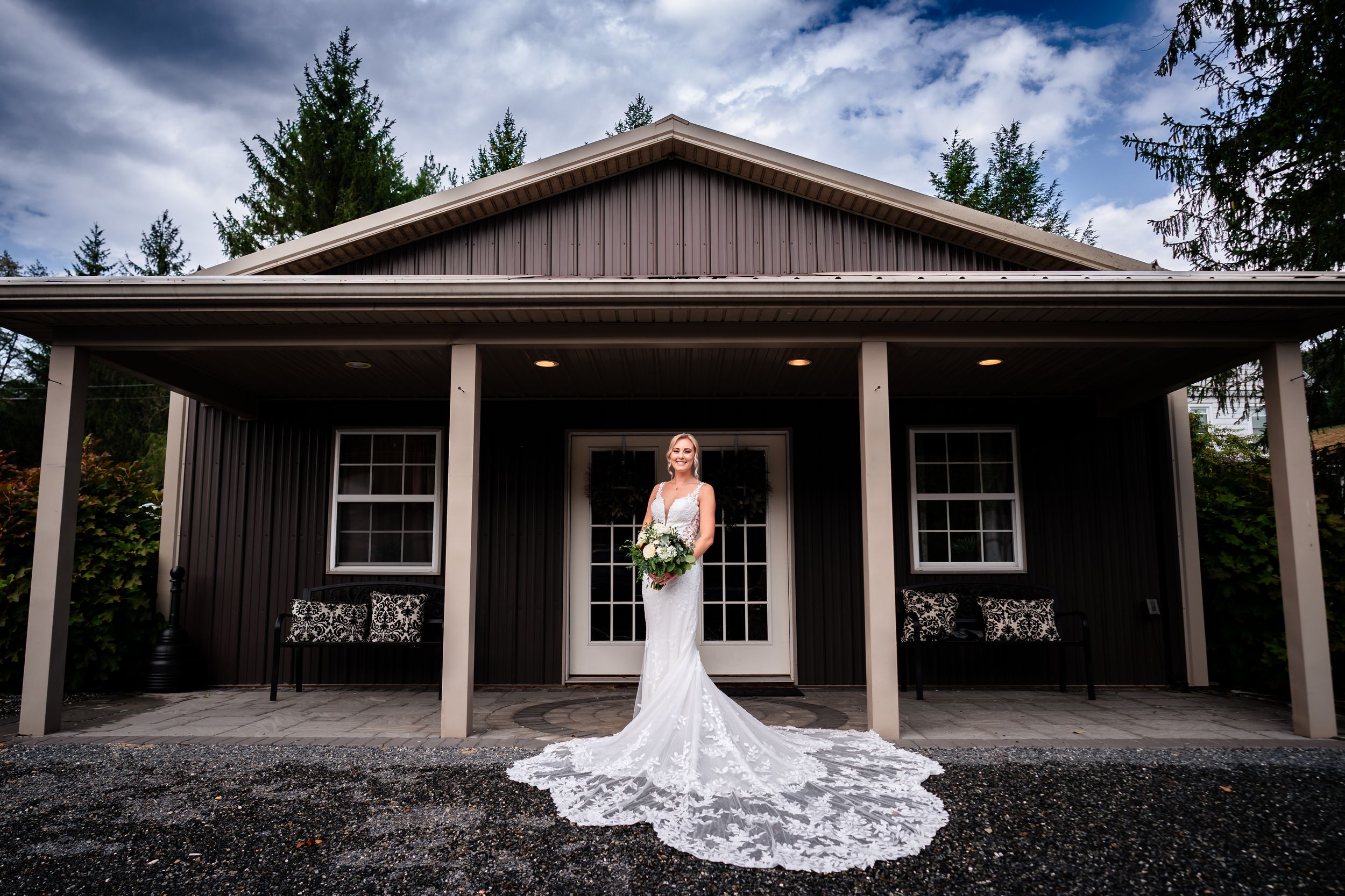 Panoramic view of a rustic wedding venue with dark clouds and pine trees in background.