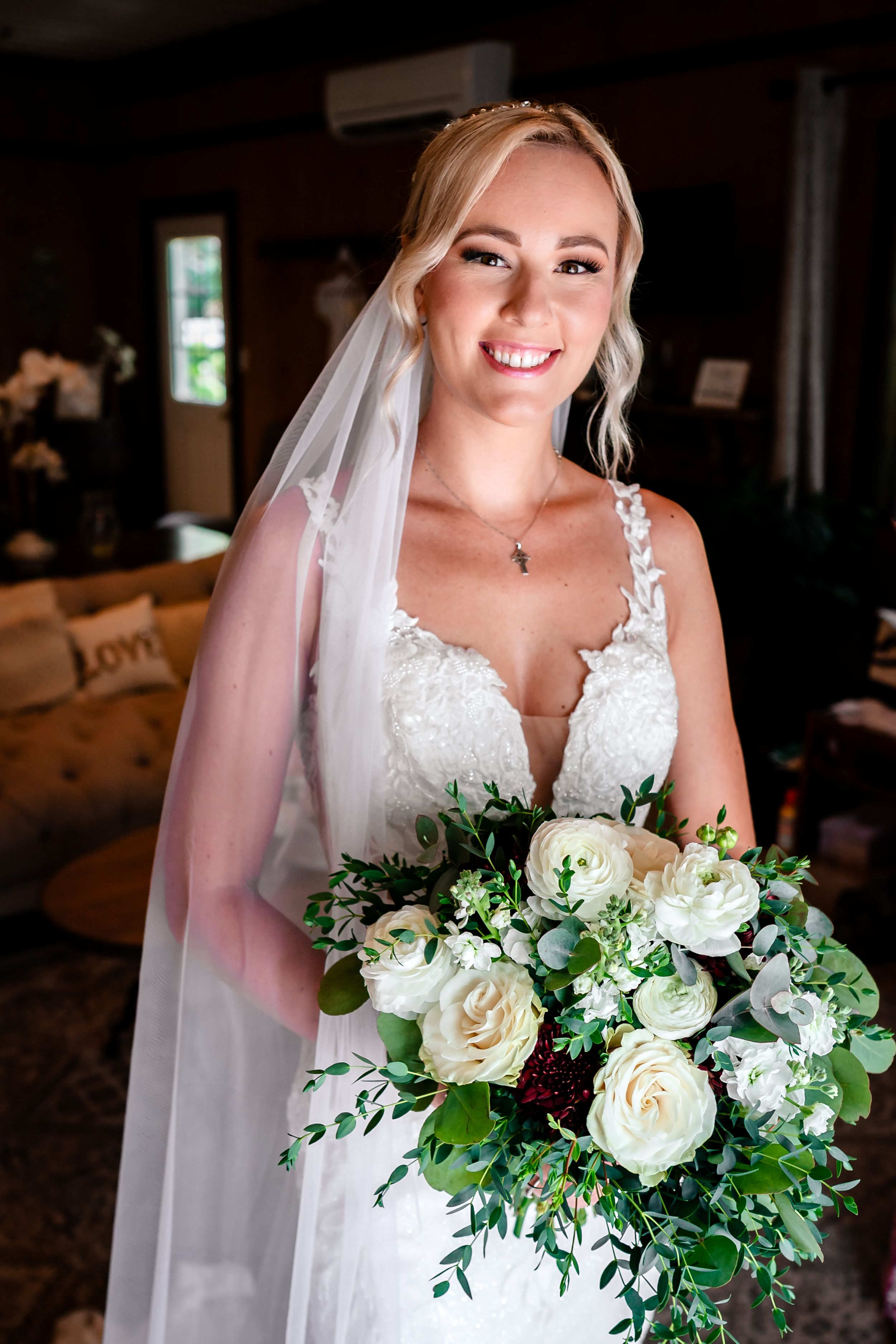 Bride holds elegant white and green bouquet while wearing lace wedding dress and veil.