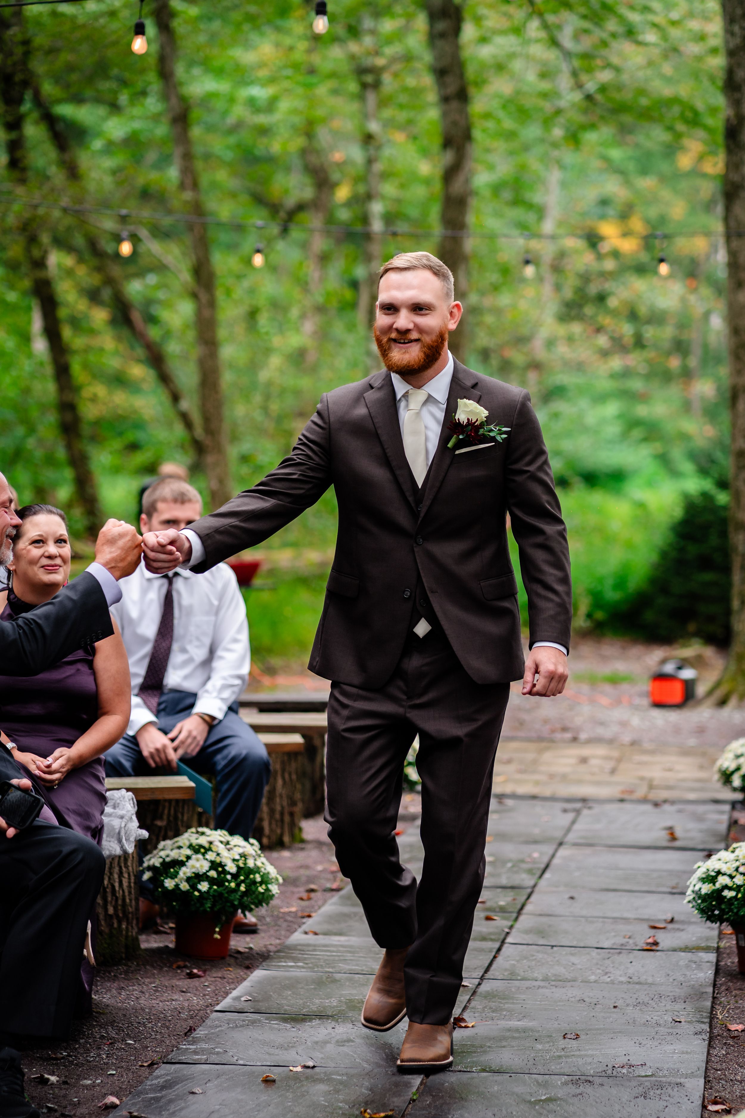 Wedding party members in dark suits sharing a lighthearted moment on a wooden walkway.