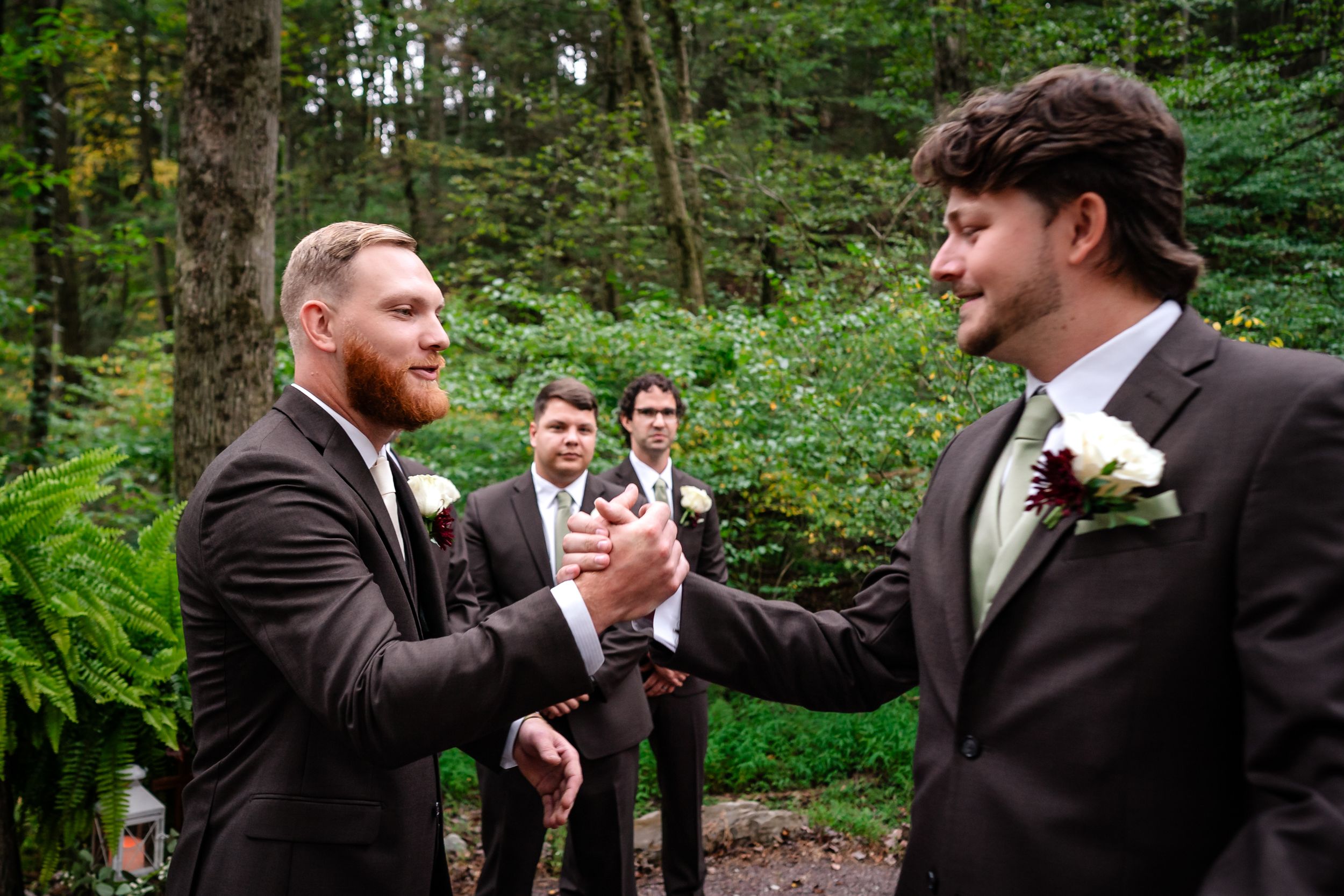 Groomsmen in dark suits laughing together during outdoor wedding celebrations.