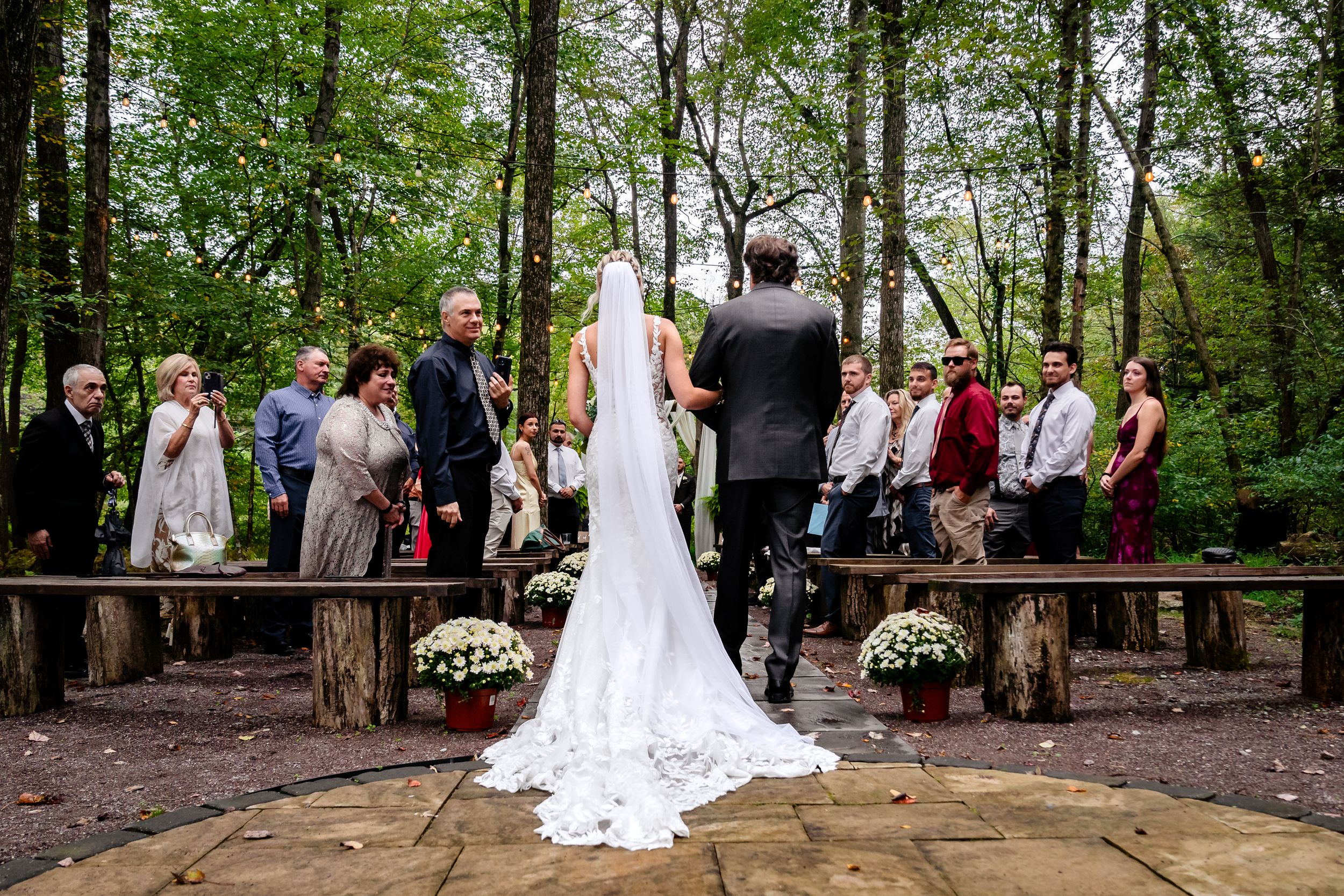 Forest wedding ceremony setup with wooden walkway and white floral decorations.