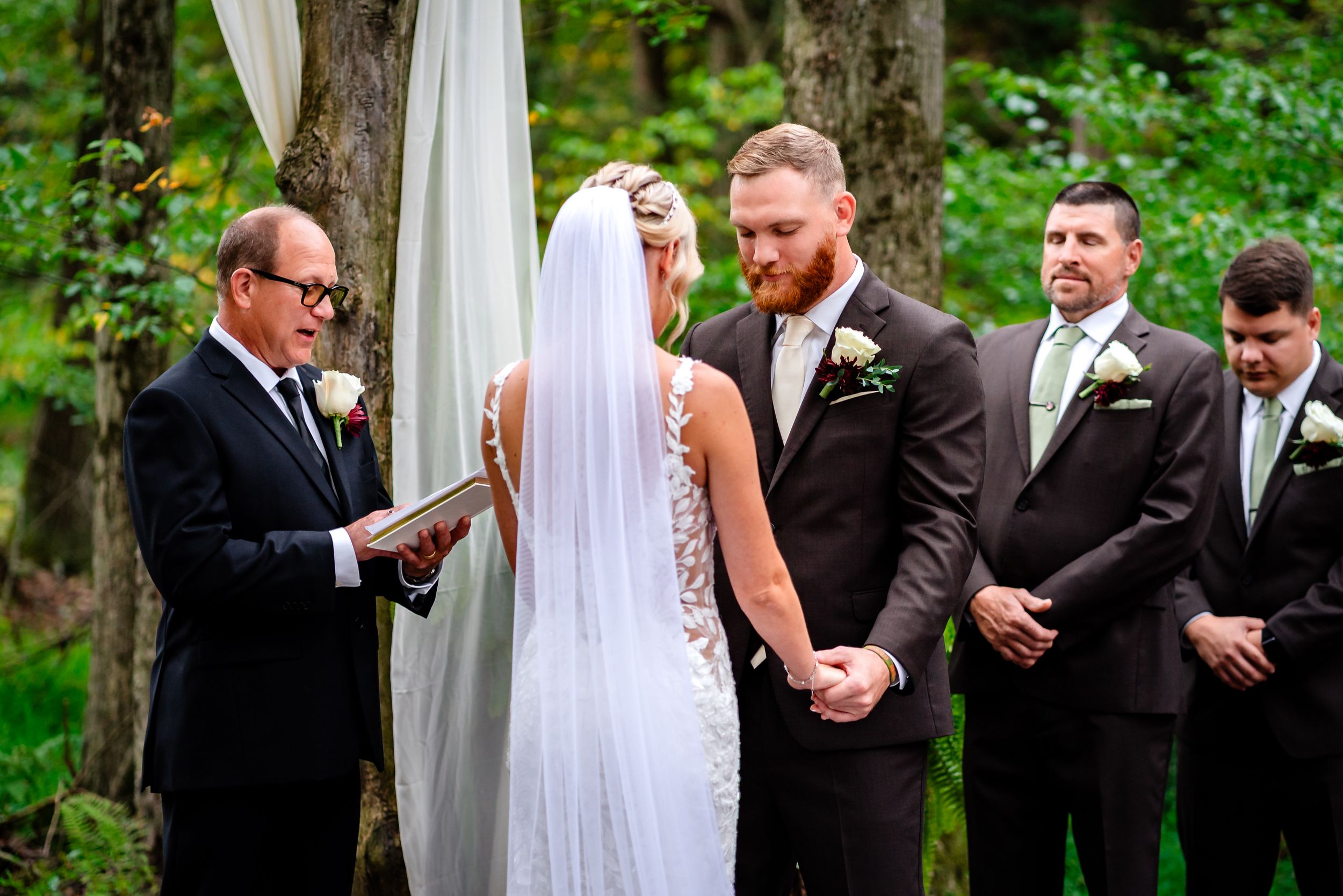 Wedding ceremony proceedings in a natural forest setting with white draping and decor.