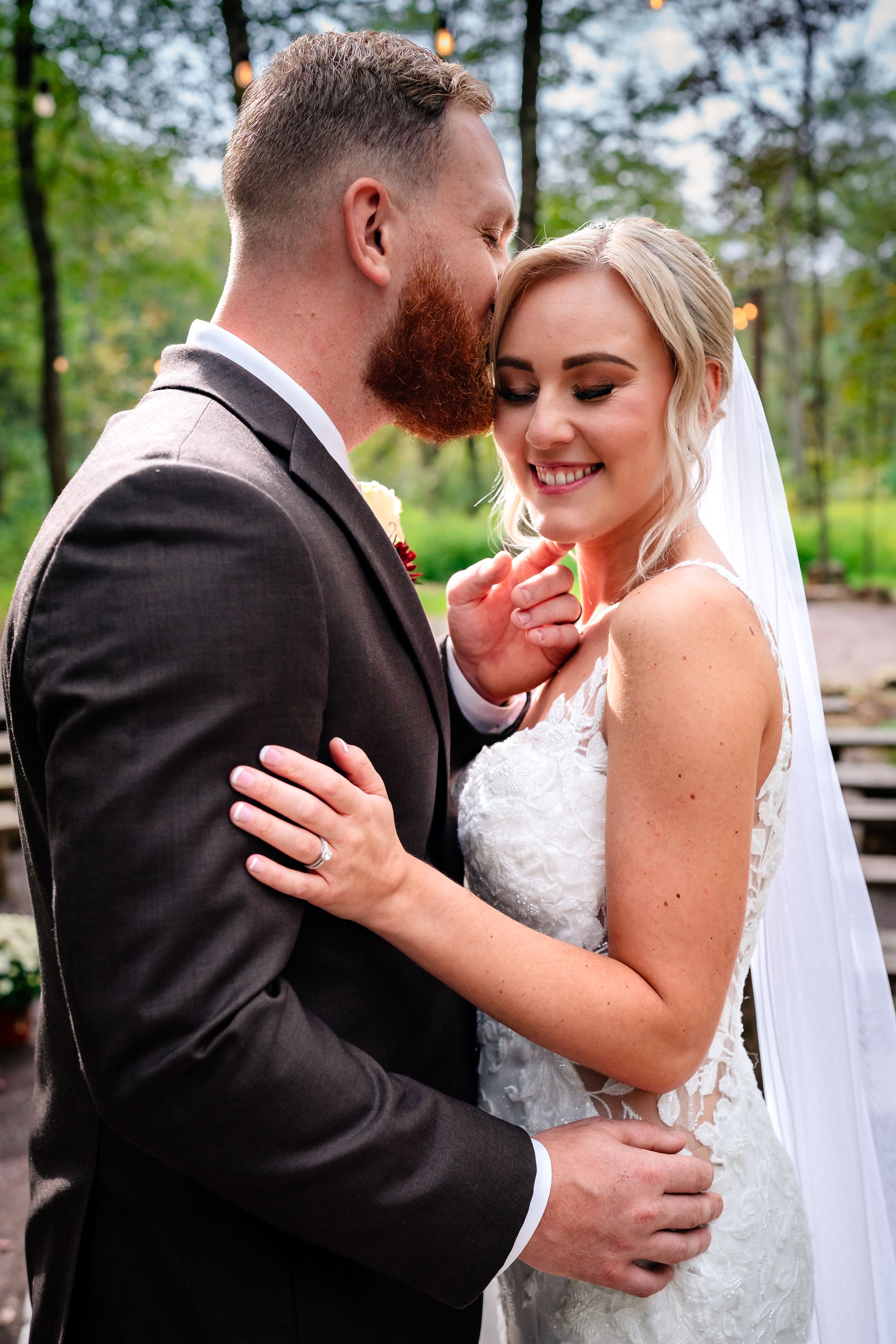 Intimate romantic moment between couple in formal wedding attire in forest setting.
