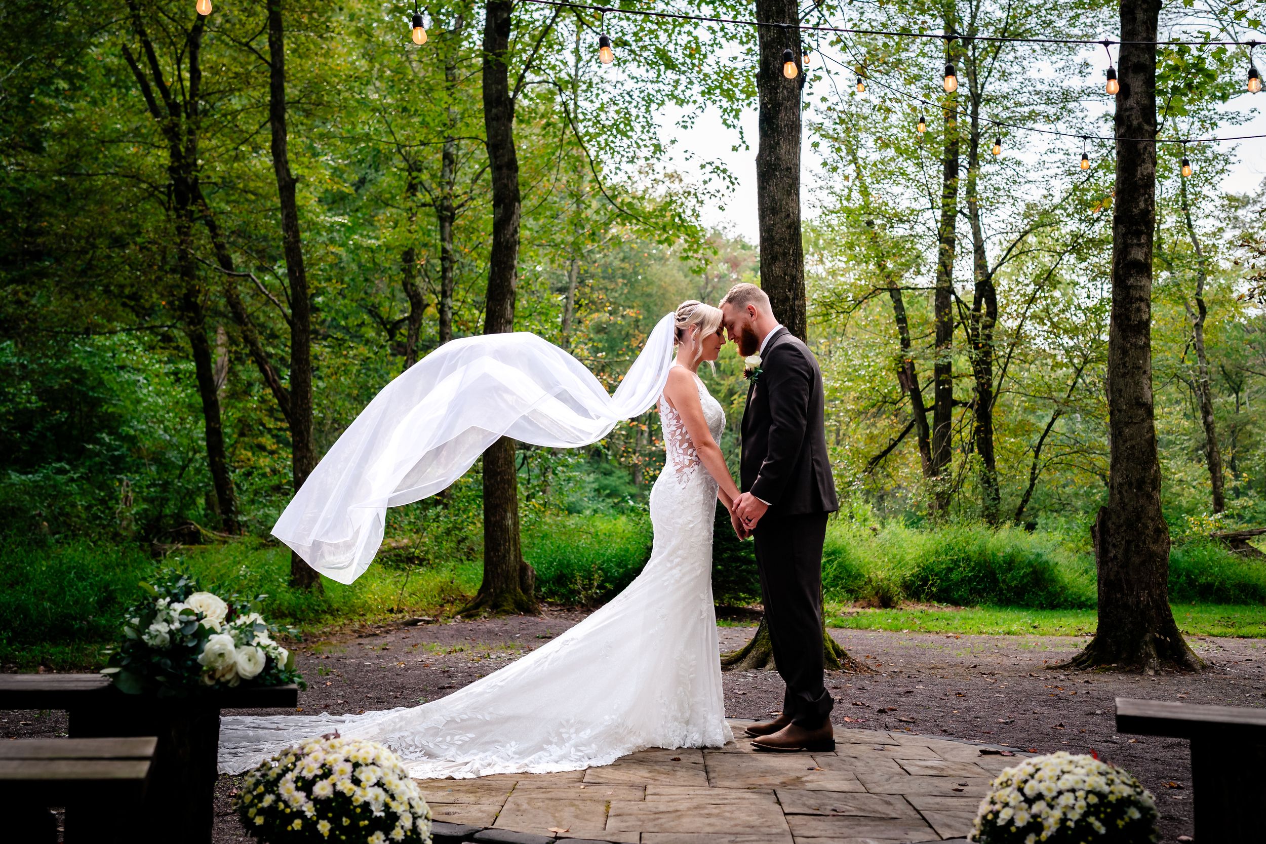 Dramatic wedding portrait with flowing veil in wooded setting on stone patio.