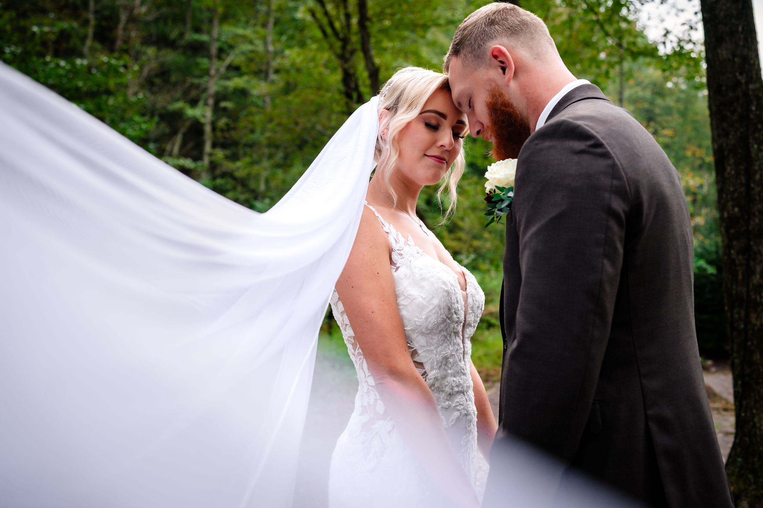 A couple shares a romantic moment outdoors surrounded by lush greenery.