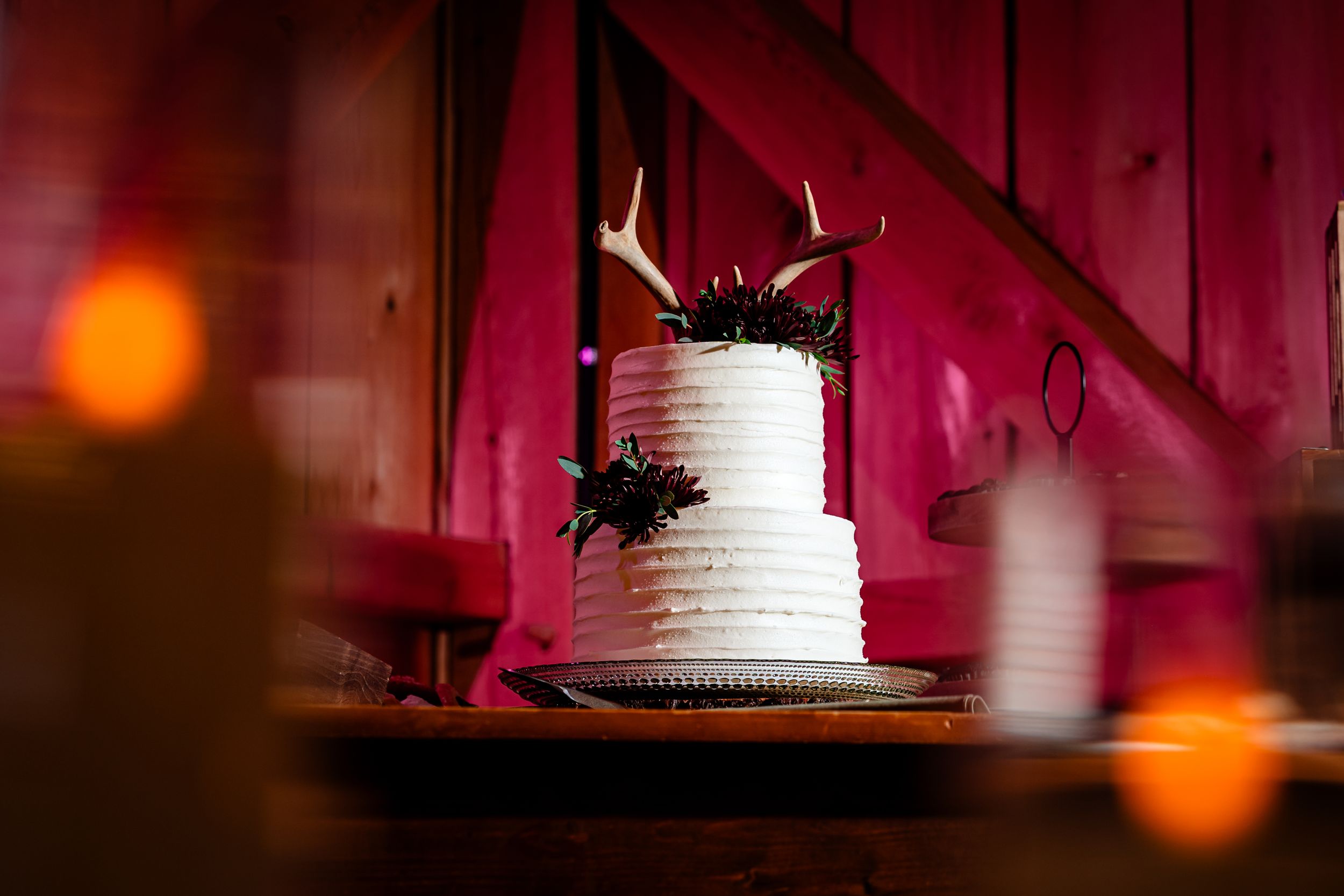 Wedding cake displayed on rustic wooden table with dramatic red lighting and bokeh effects.