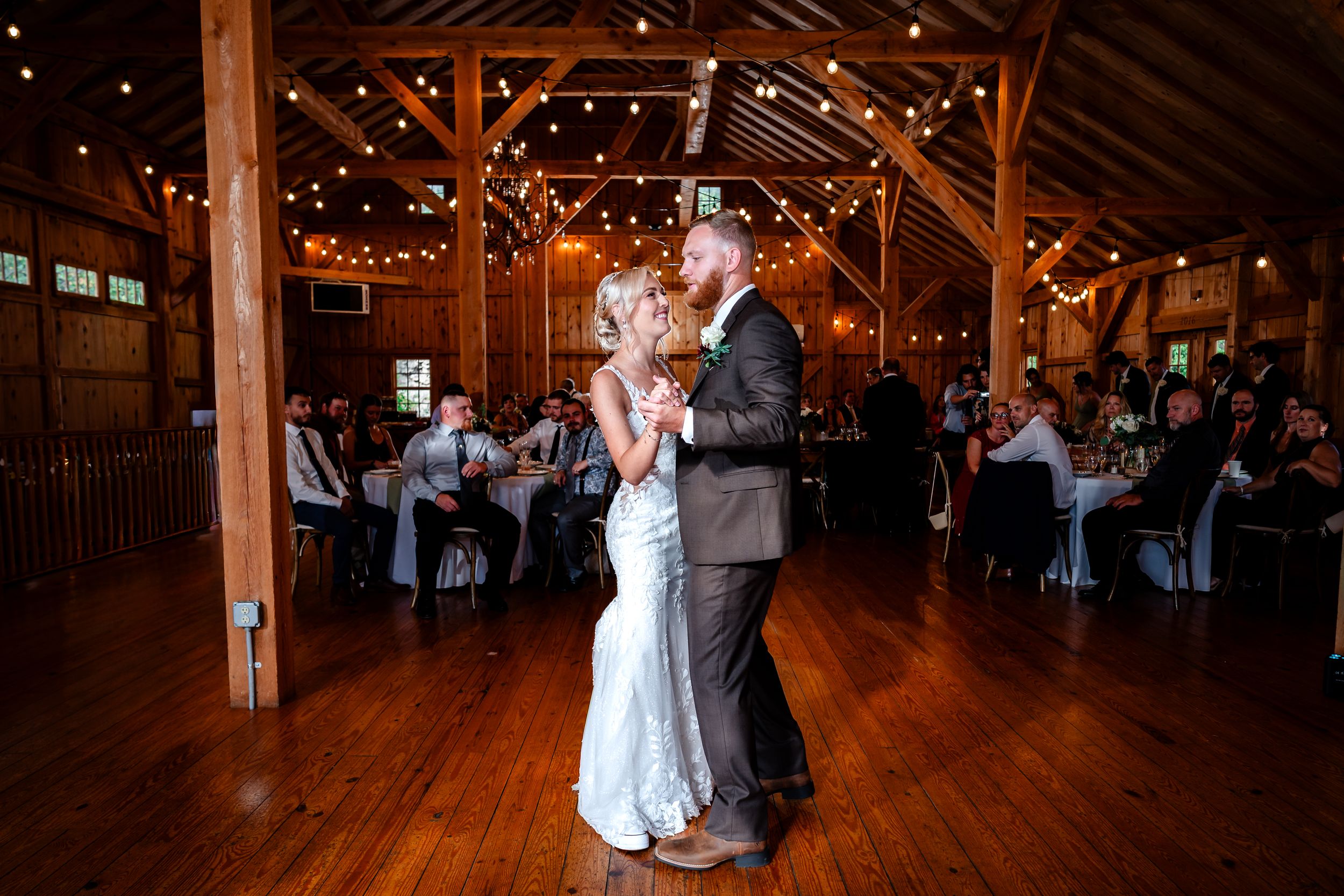 Wedding reception dance floor in rustic barn venue with string lights overhead.