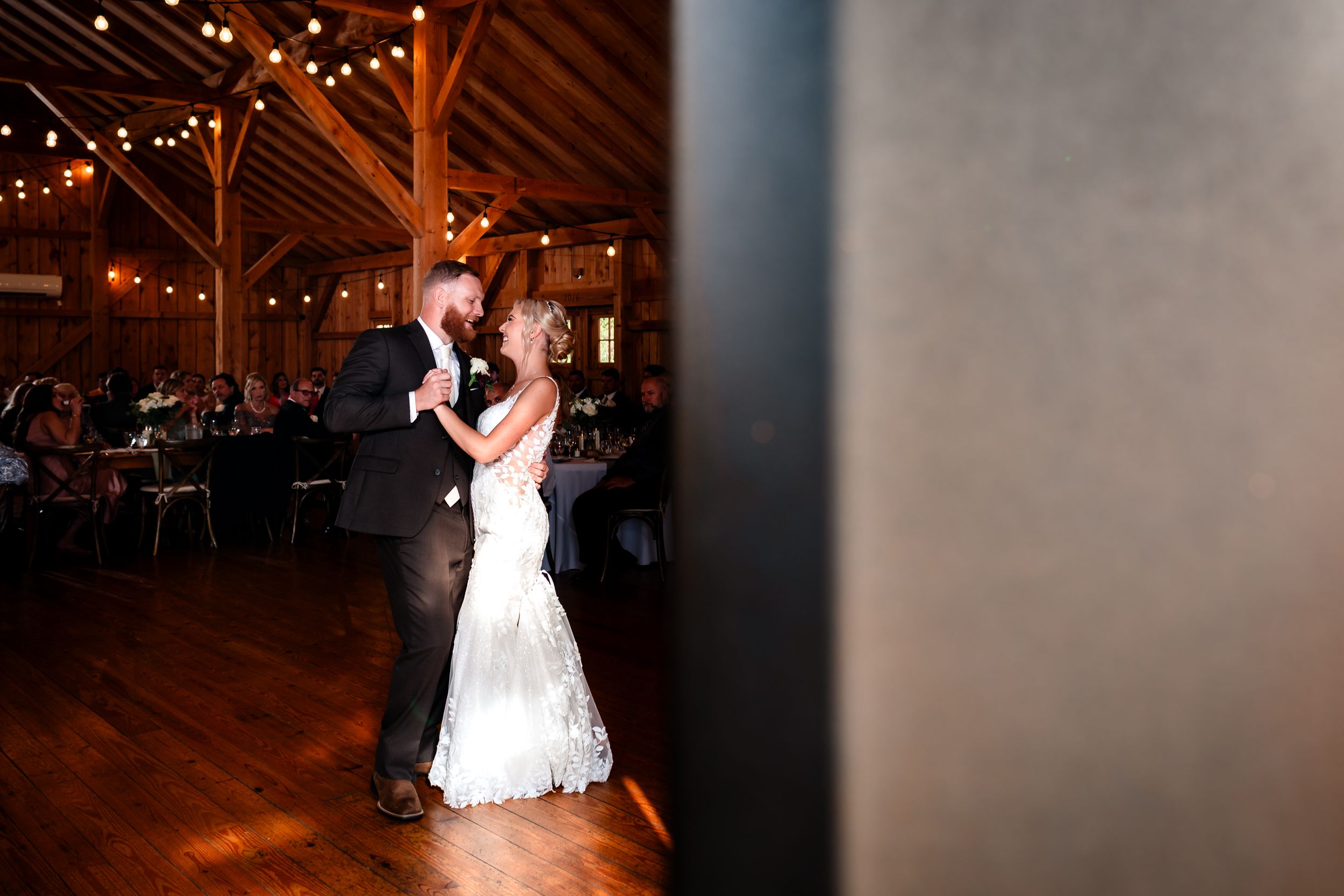 First dance moment in rustic barn venue with warm lighting and wooden beams.