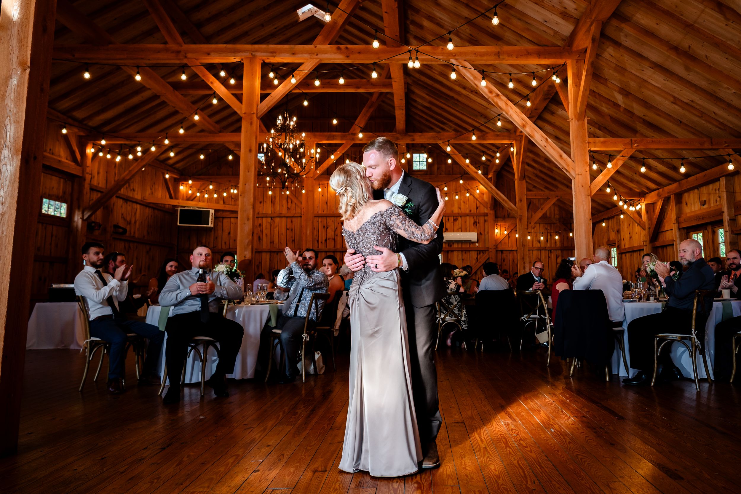Wedding celebration in rustic barn venue with dancing couples and string lights.