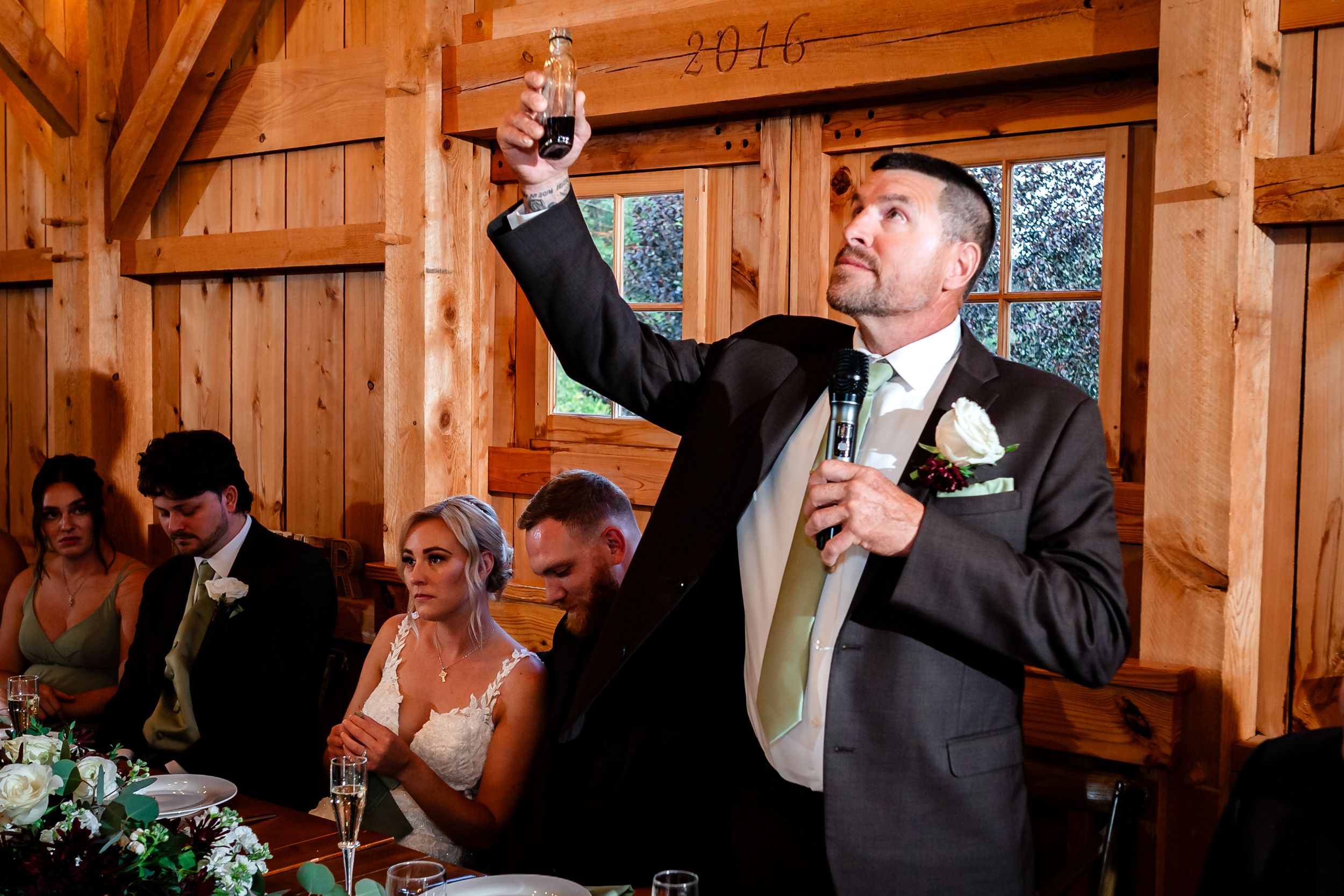 Wedding toasts and speeches in rustic wooden barn venue with natural lighting.