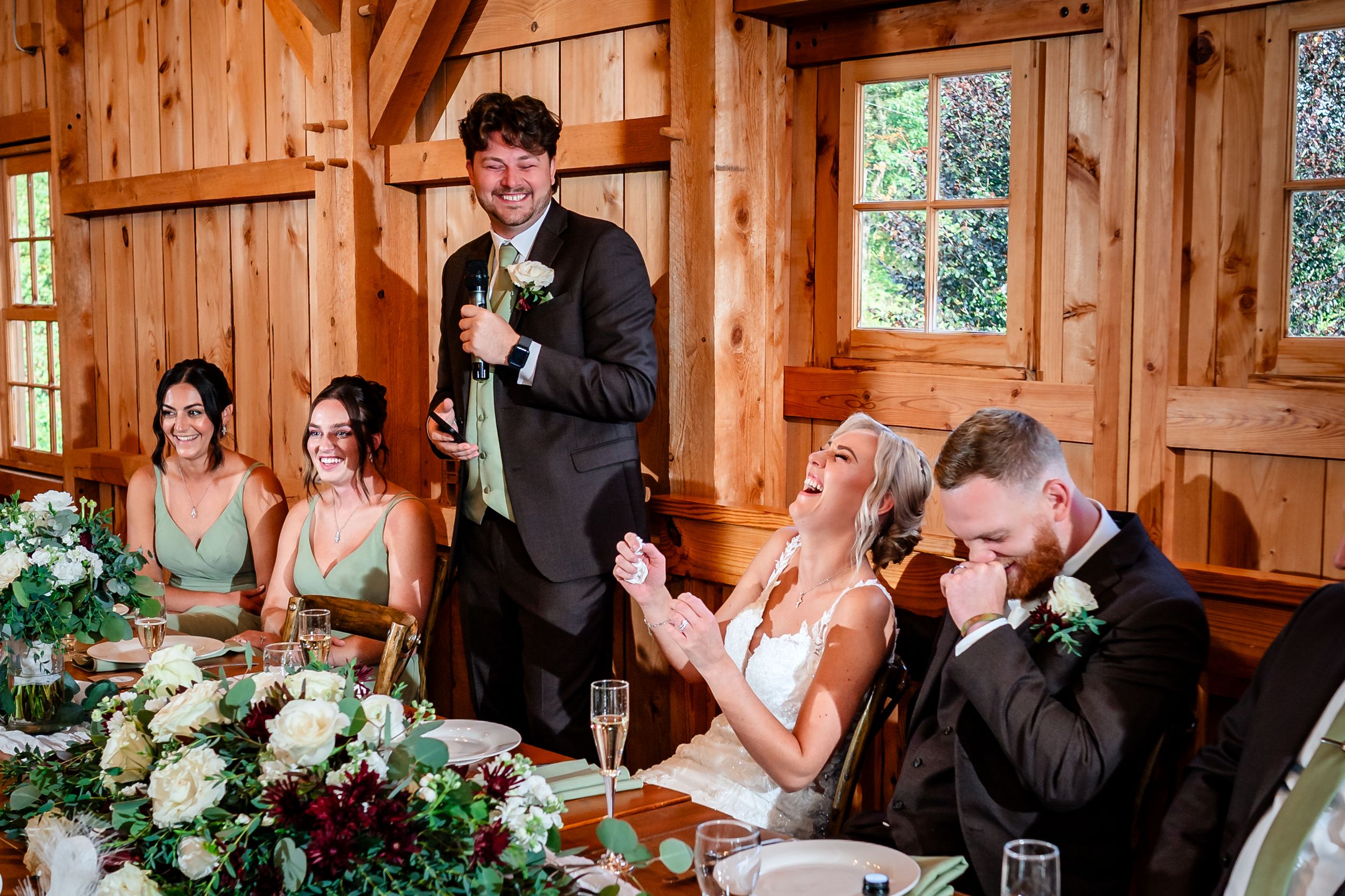 Wedding reception speeches and toasts in elegant timber frame venue with floral decorations.