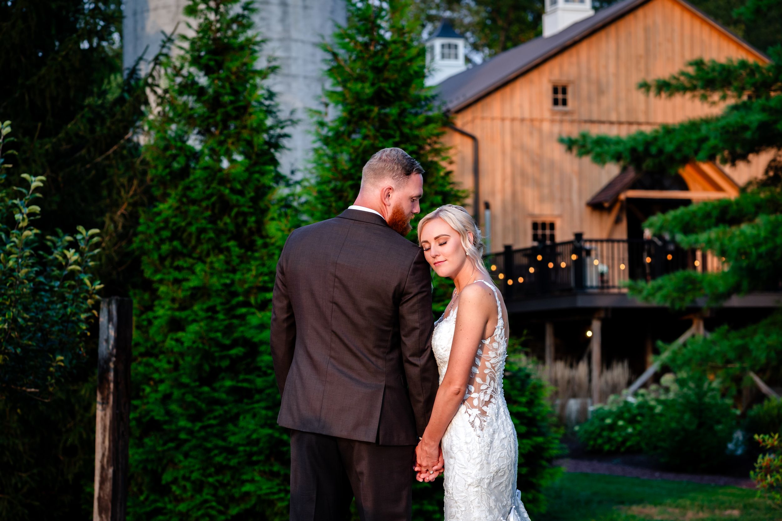 Evening wedding portraits with rustic orange barn and evergreen trees in background.