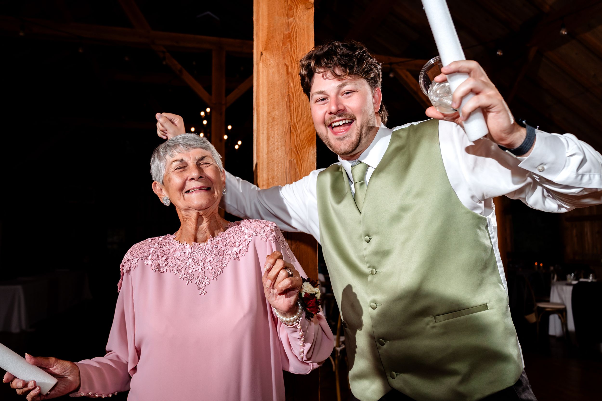 Wedding reception inside a warmly lit wooden barn with exposed beams and festive lighting.