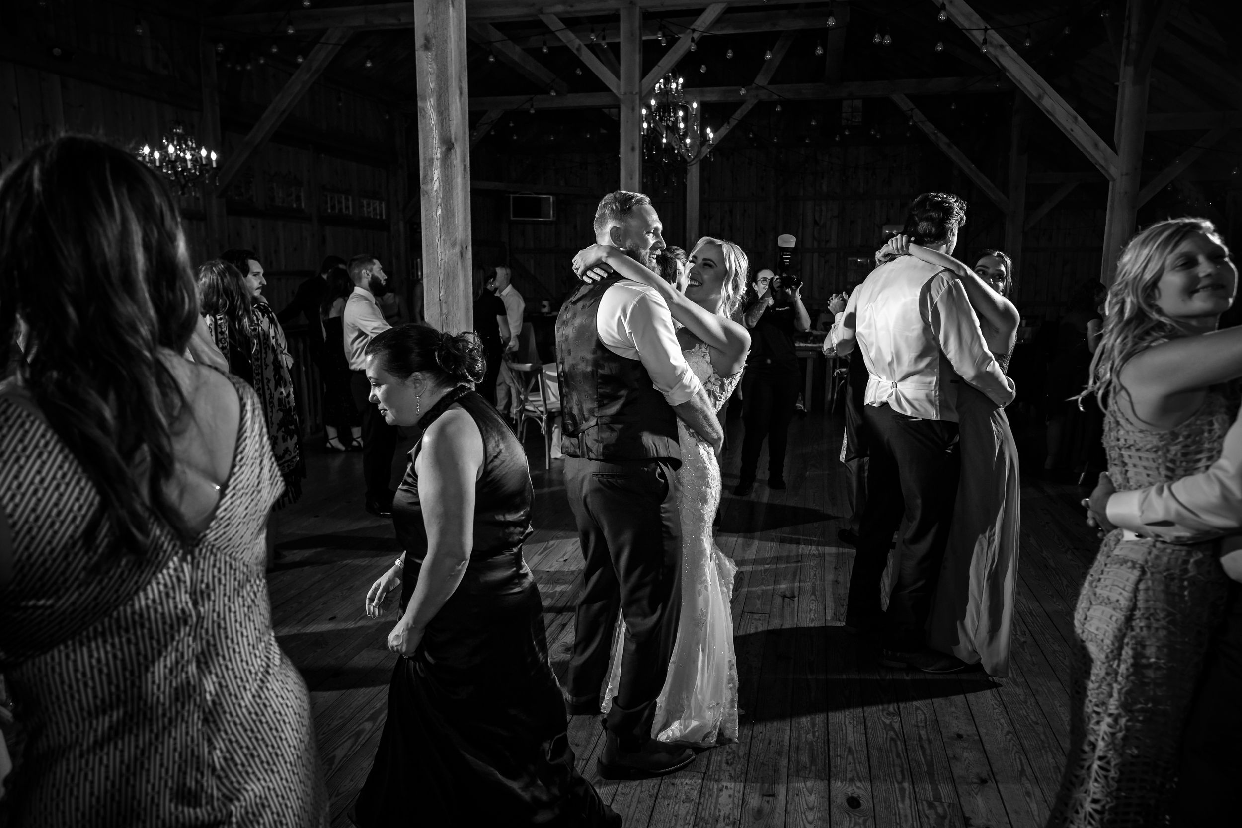 Wedding guests dancing in a dimly lit barn during an evening reception celebration.