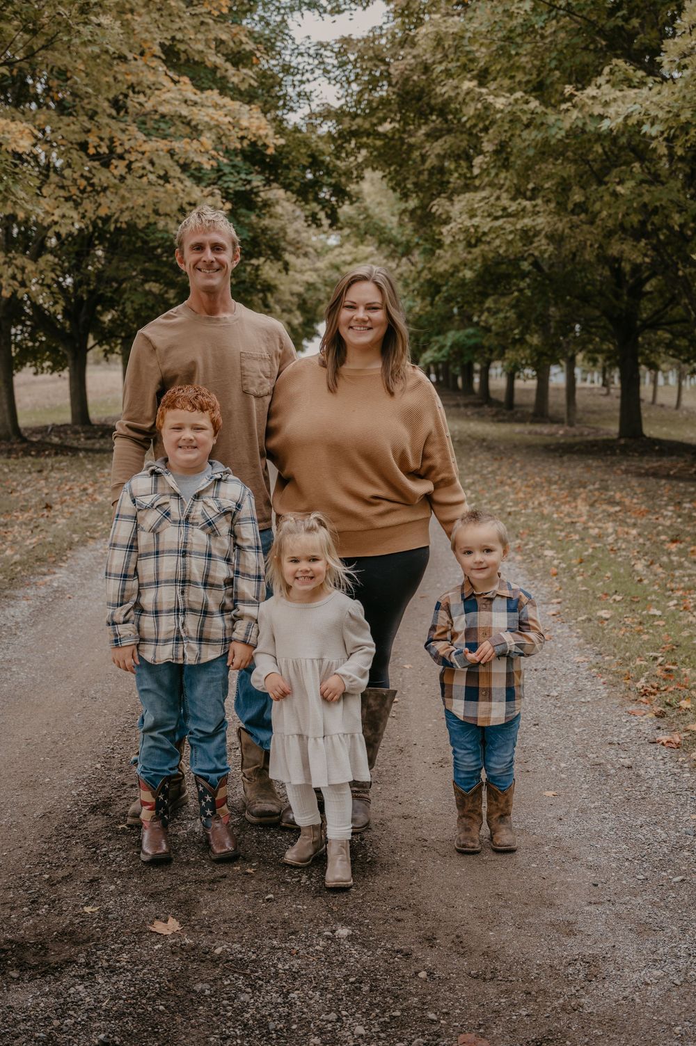 Family of five in earth tones walks along a tree-lined path during autumn family portrait session.